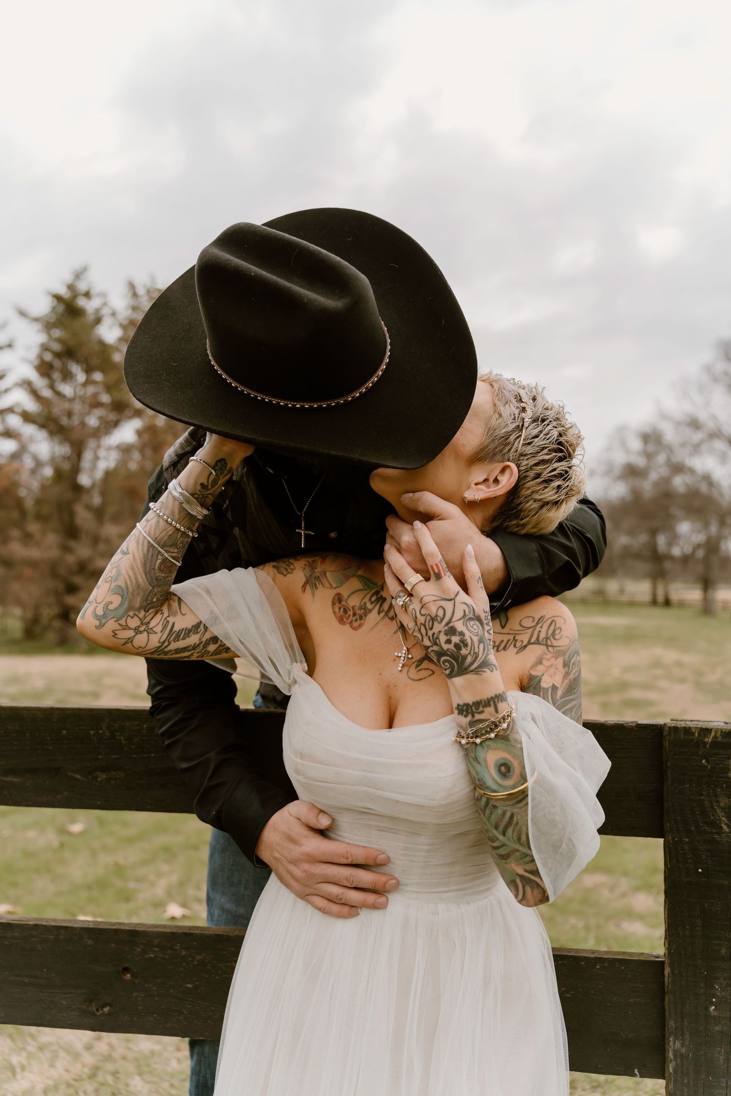 A romantic wedding moment captured with a cowboy hat against a rustic fence.