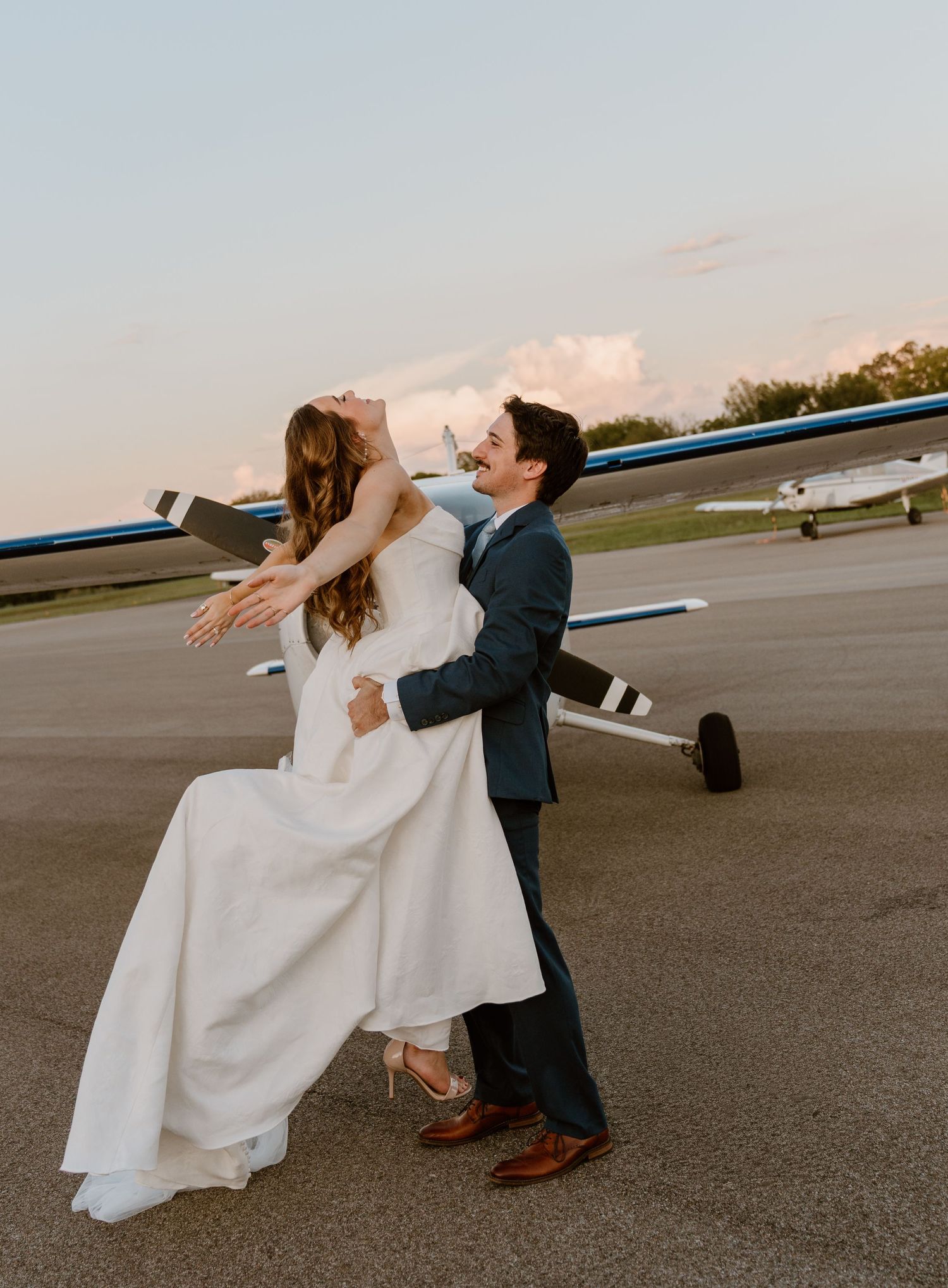 A dramatic dip pose on an airport runway with a small plane in the background.