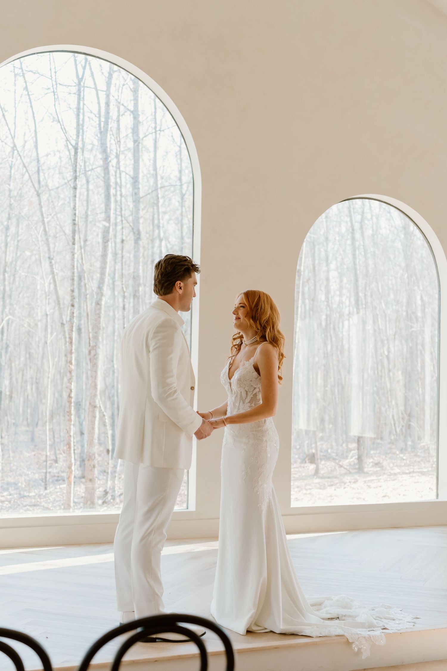 A romantic first look sequence in a bright room with arched windows overlooking a winter forest.
