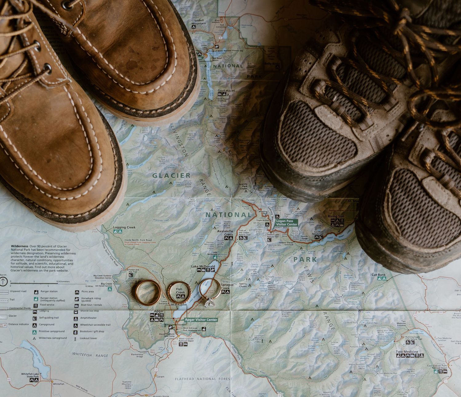 Wedding rings and hiking boots placed on a topographic map, suggesting adventure and outdoor wedding planning.