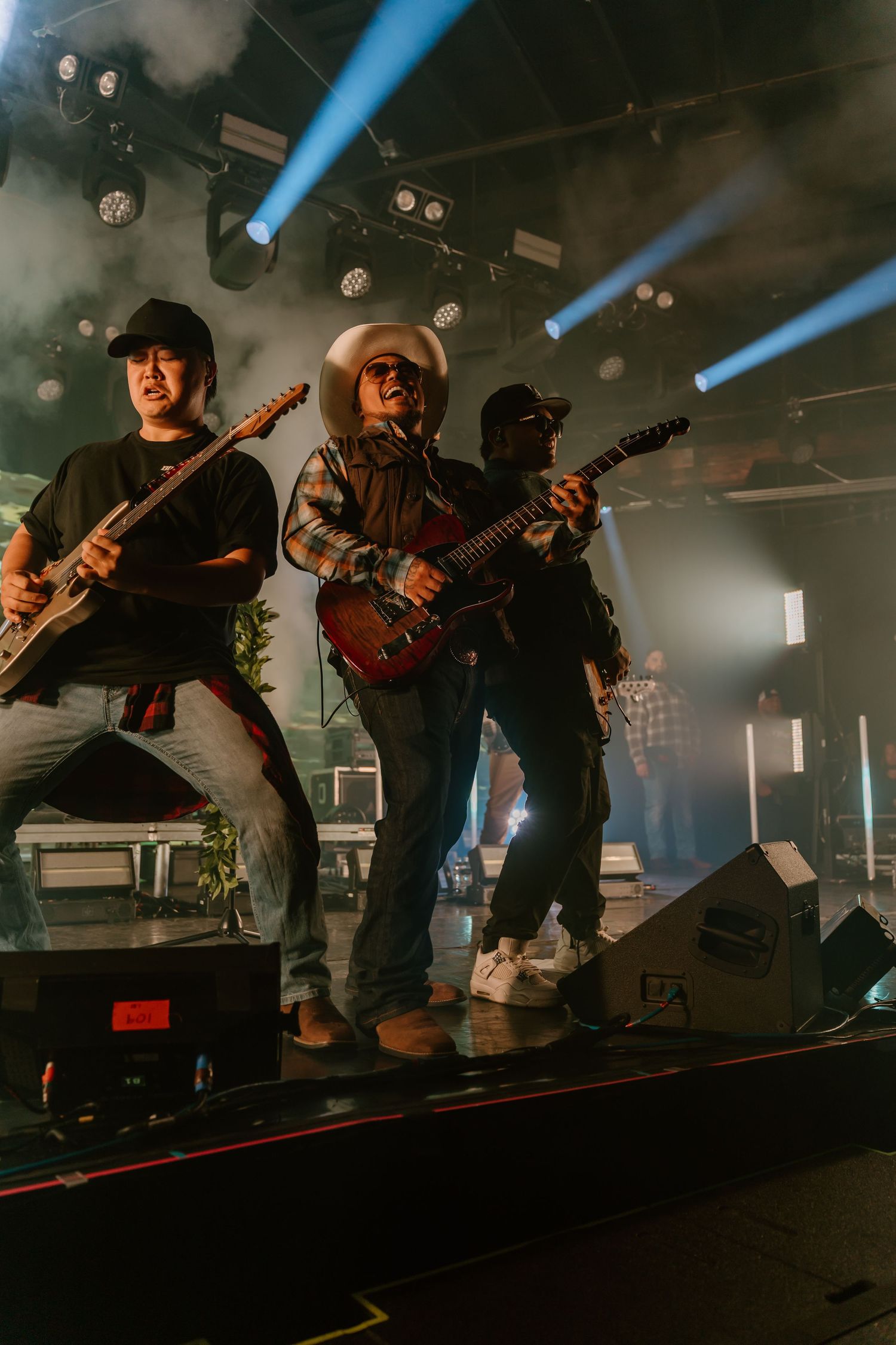 Musicians perform on a dimly lit stage with dramatic blue lighting and atmospheric smoke effects.