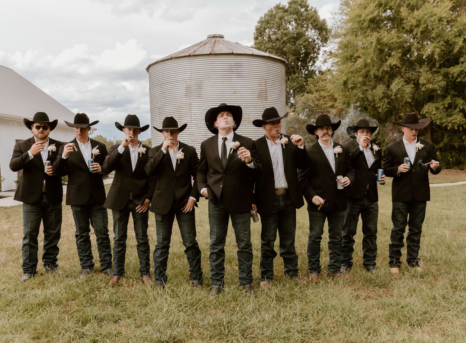 Groomsmen in black suits and cowboy hats stand in a line outdoors for a wedding photo.