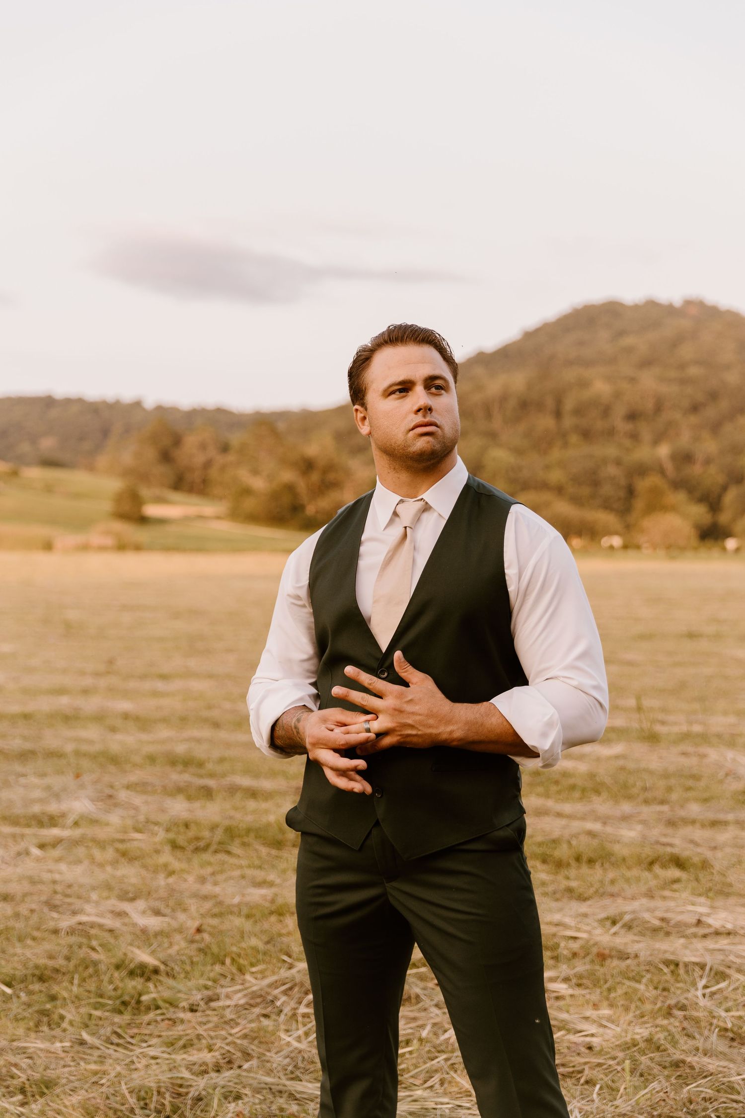 Wedding party member in vest and dress shirt poses dramatically in an open field.
