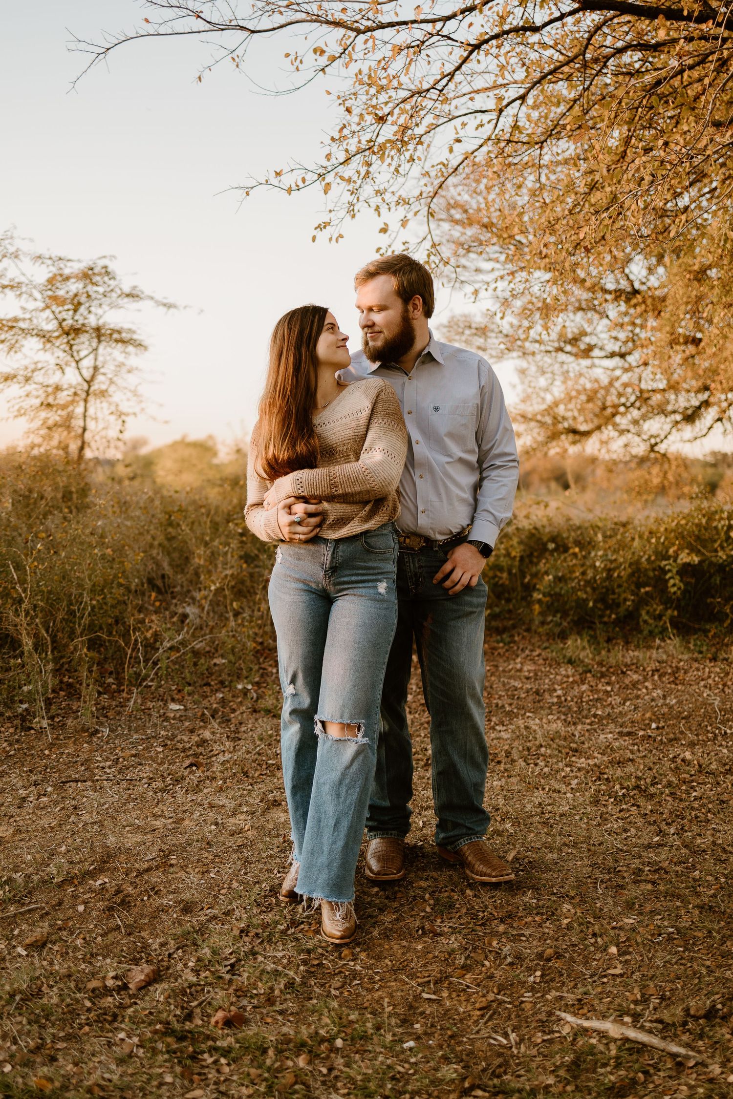 A couple embraces during sunset with autumn trees in the background.