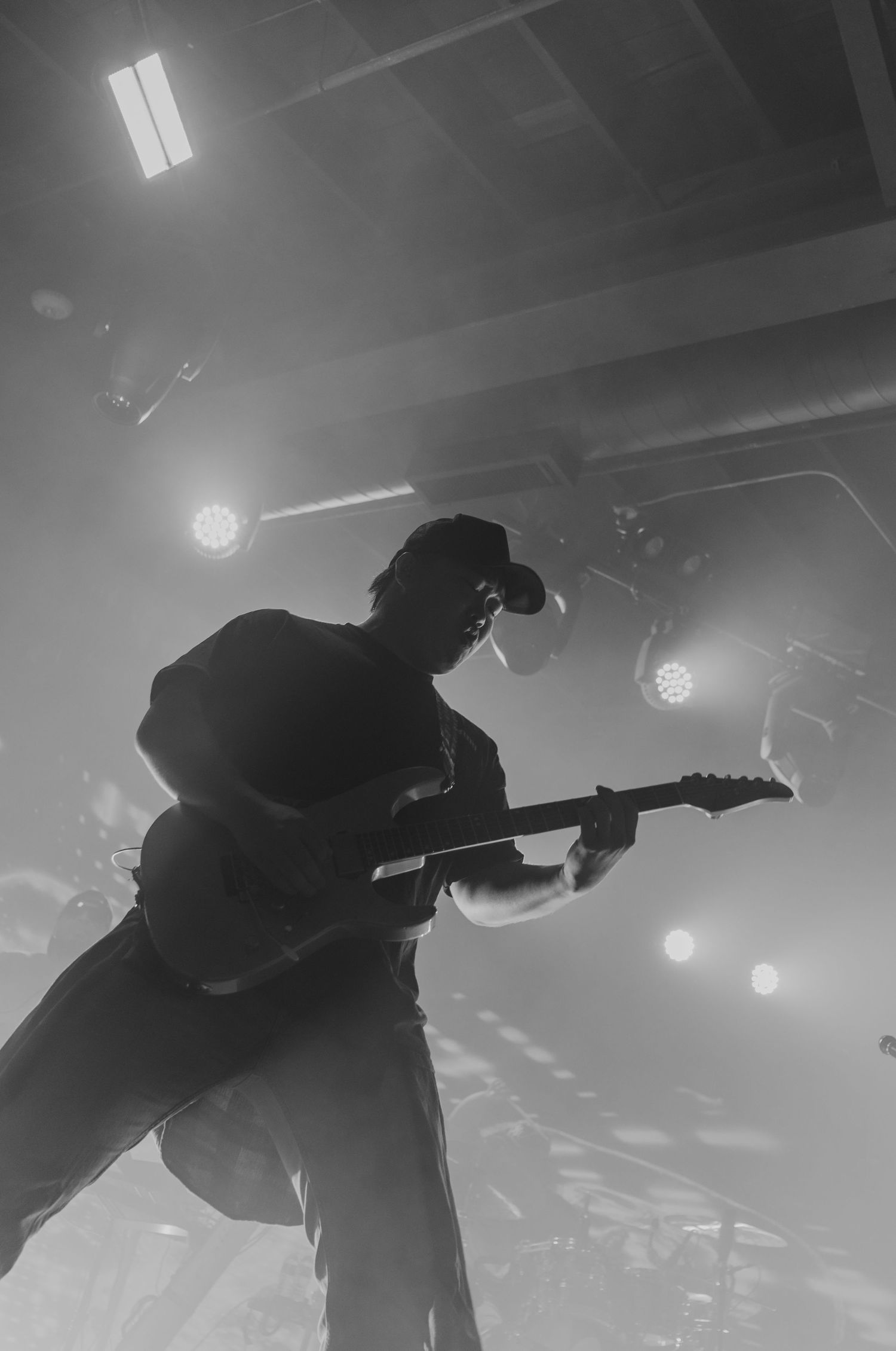 Silhouetted figures playing guitars on stage with dramatic backlighting creating moody atmosphere.