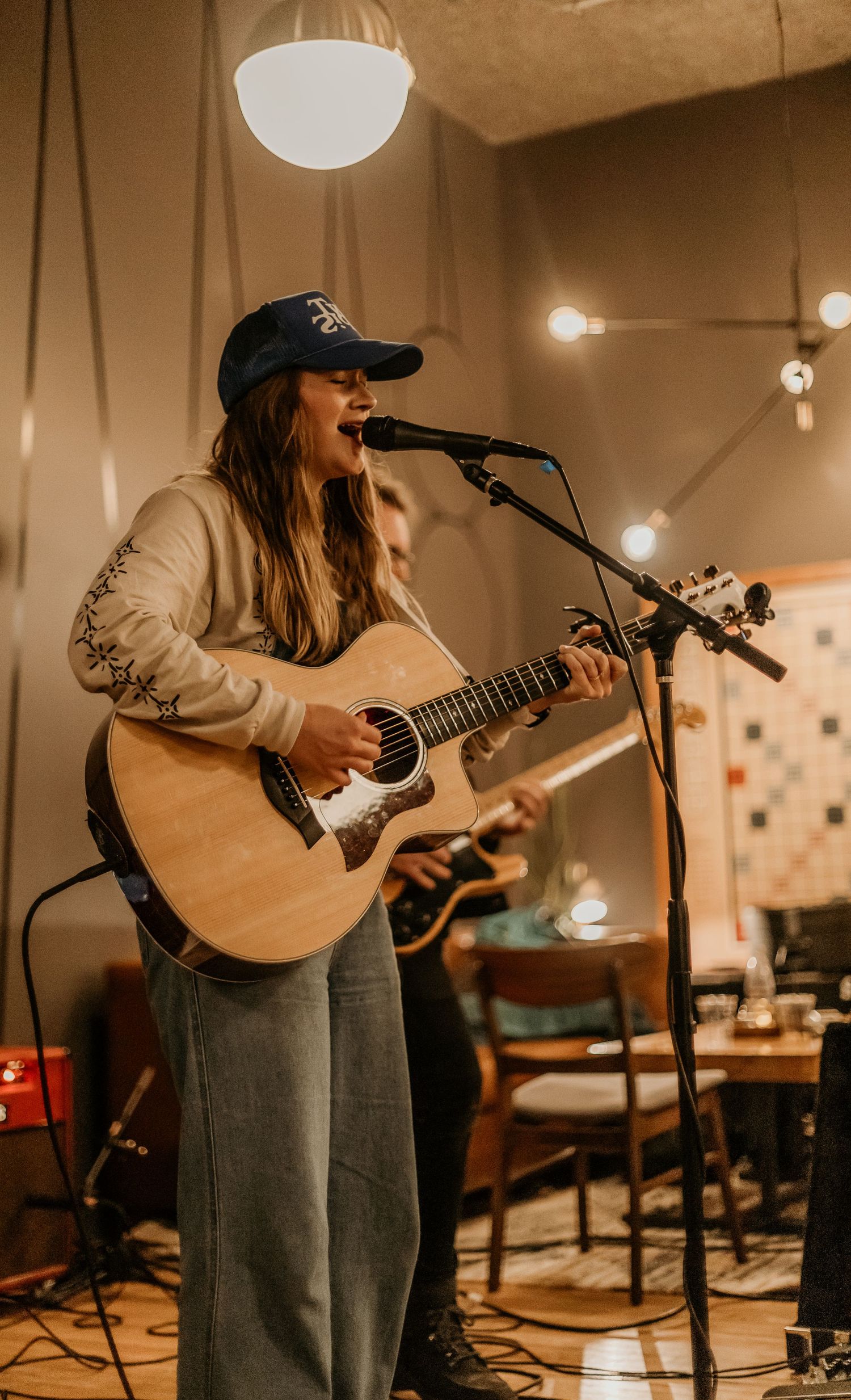 Musician plays acoustic guitar in a warmly lit indoor venue with minimalist decor.