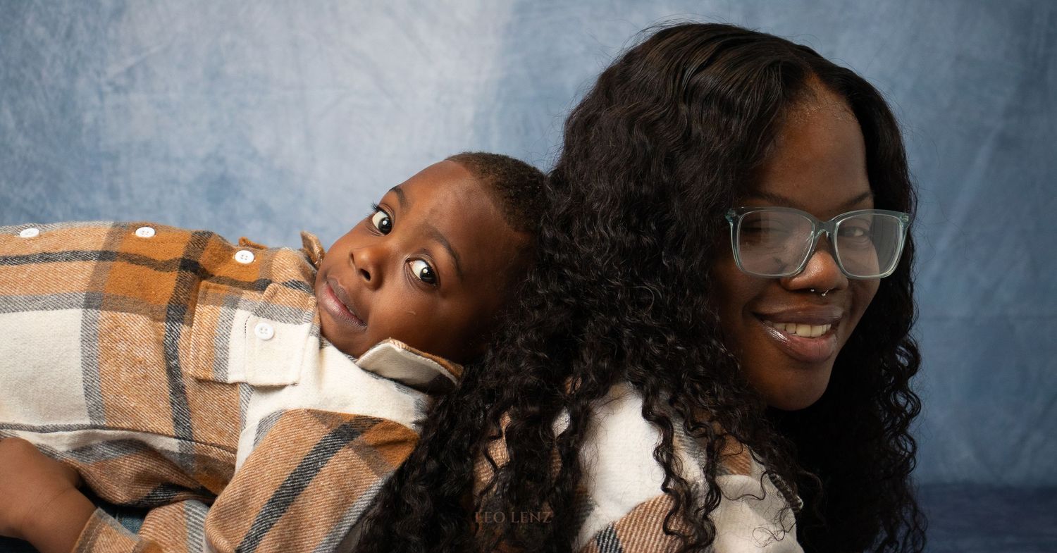 Close-up portrait of mother and child in matching plaid outfits against blue background.