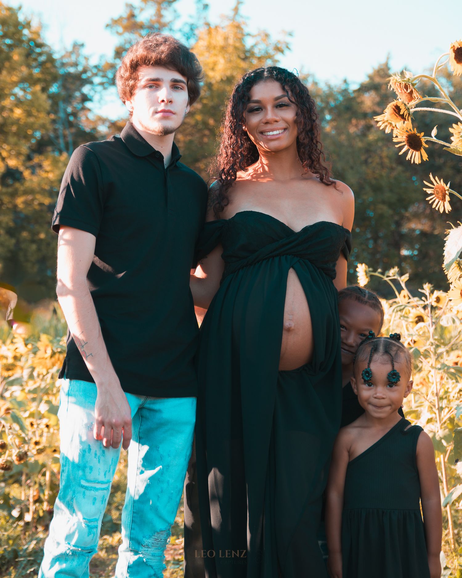 Family portrait with matching black and turquoise outfits in a sunflower field at golden hour.