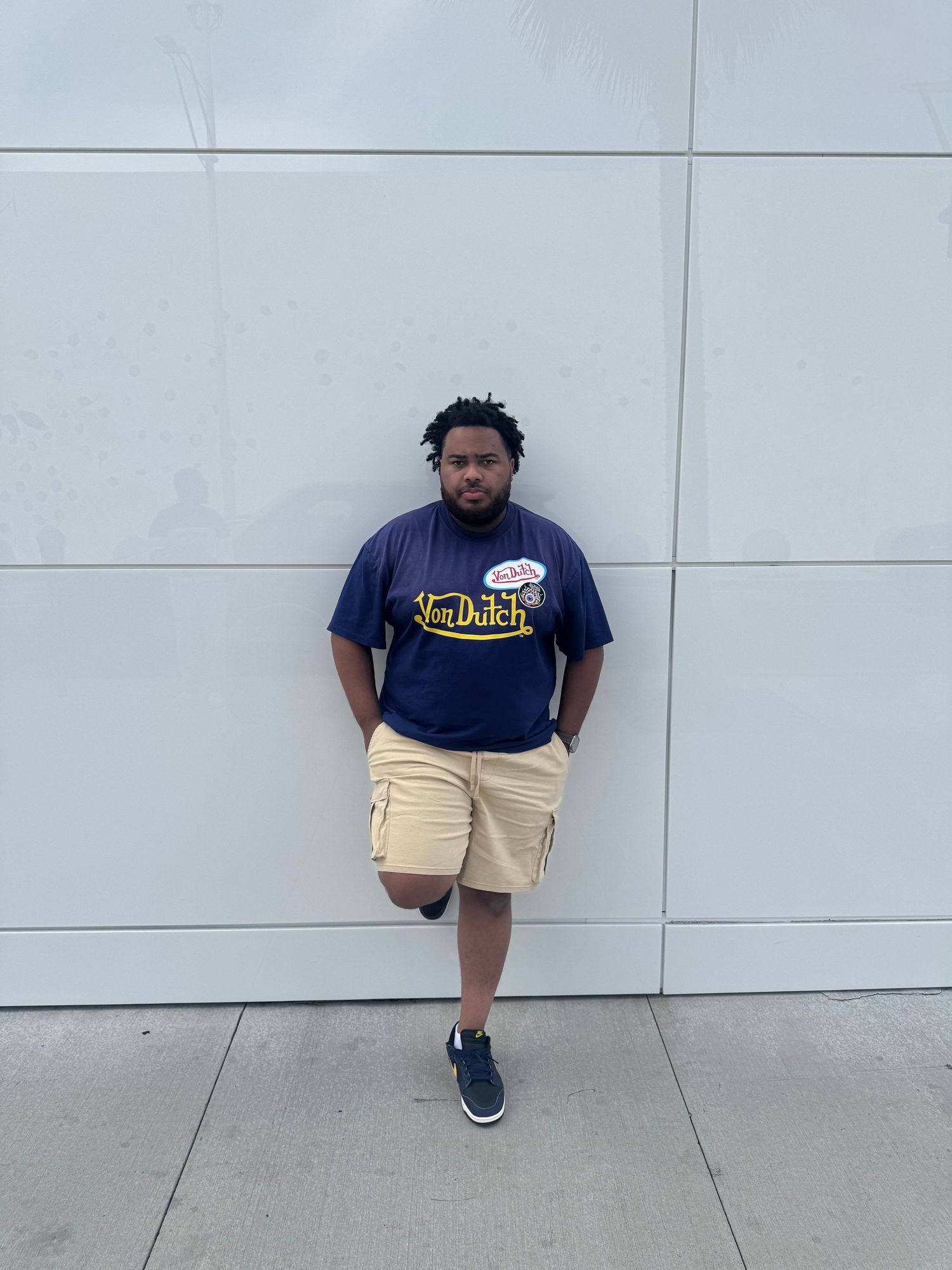 Person in navy shirt and khaki shorts posing against white wall in various stances.