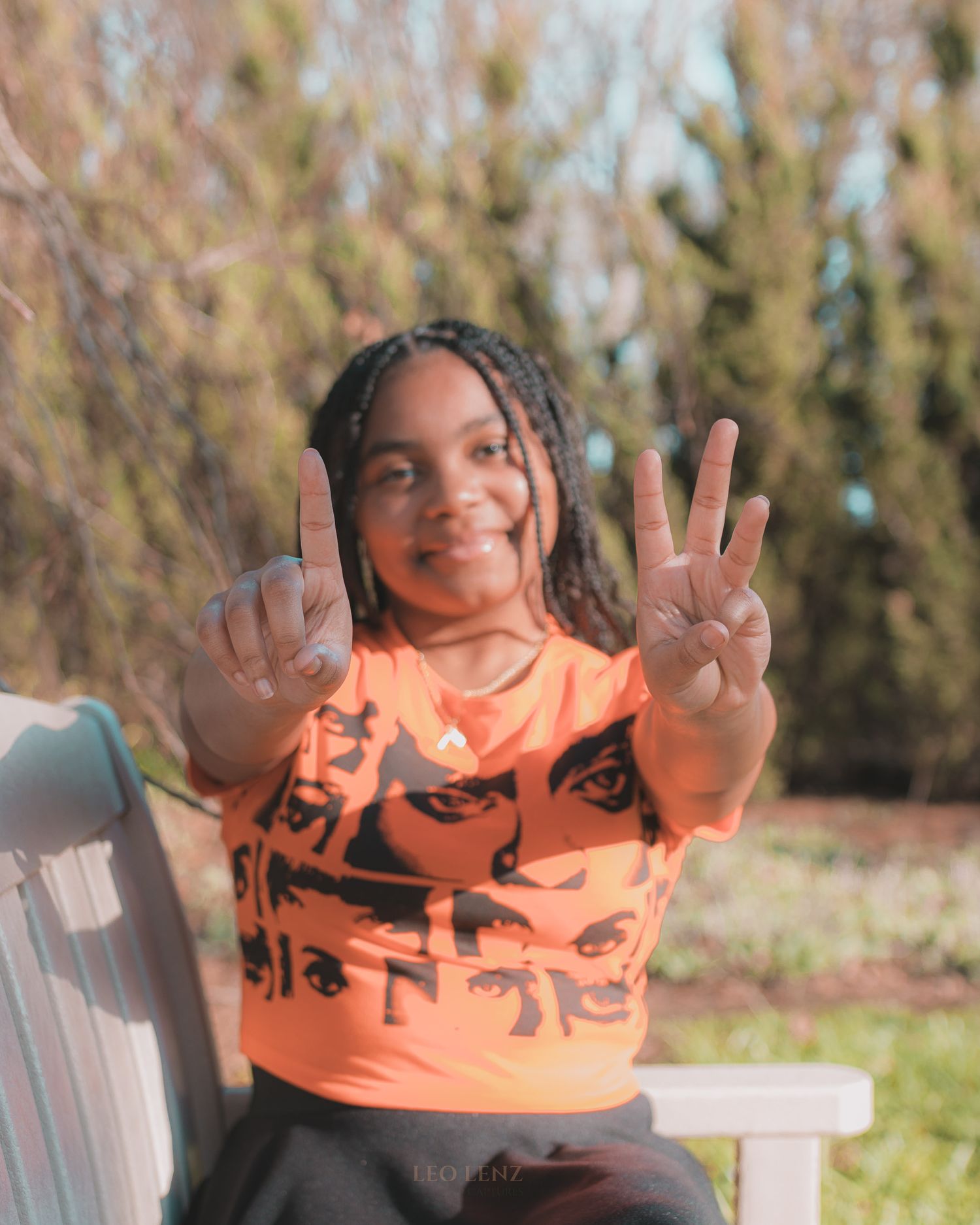 Child in bright orange t-shirt making animated gestures while sitting outdoors.