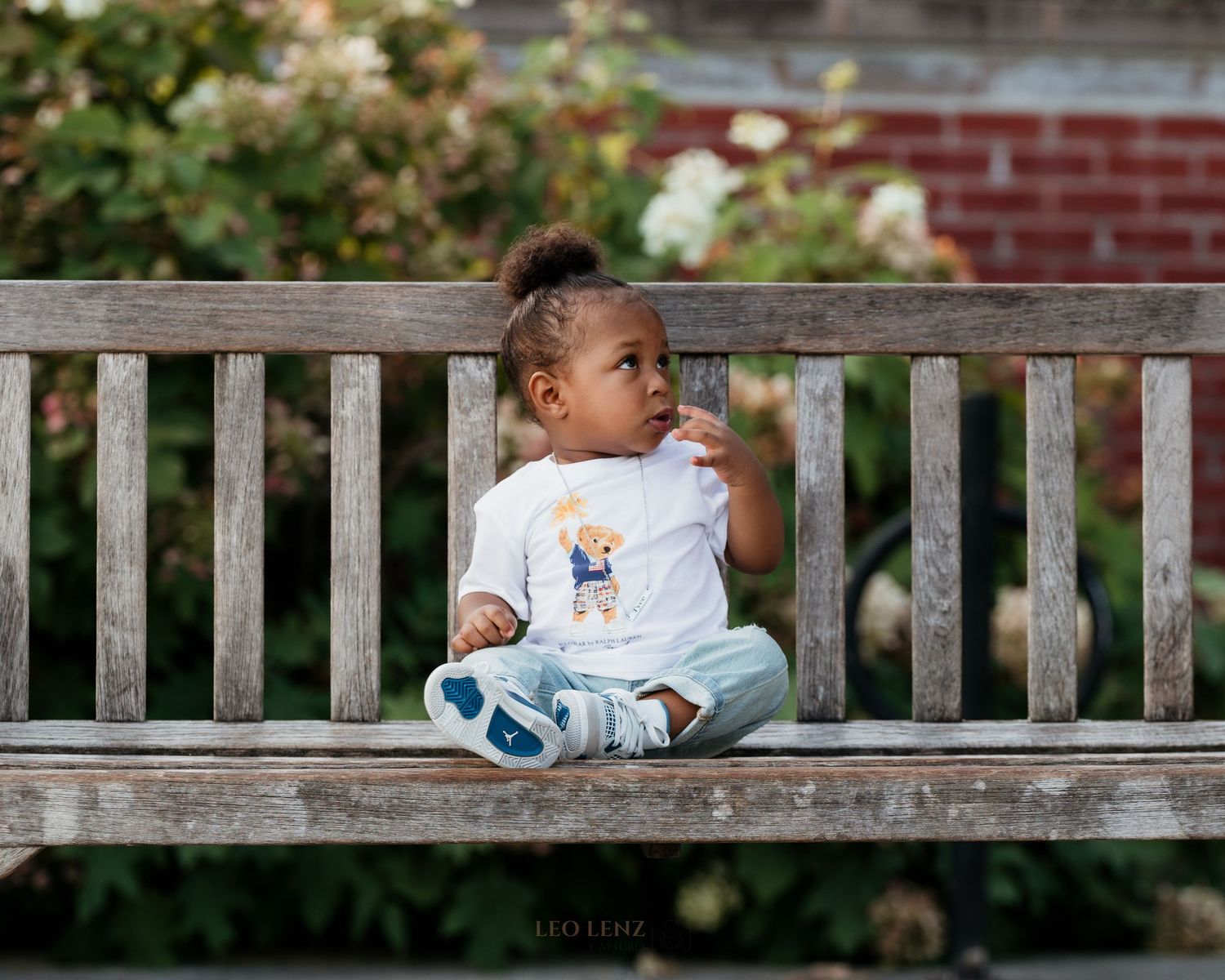 Young child sitting on wooden bench wearing white t-shirt and blue pants.