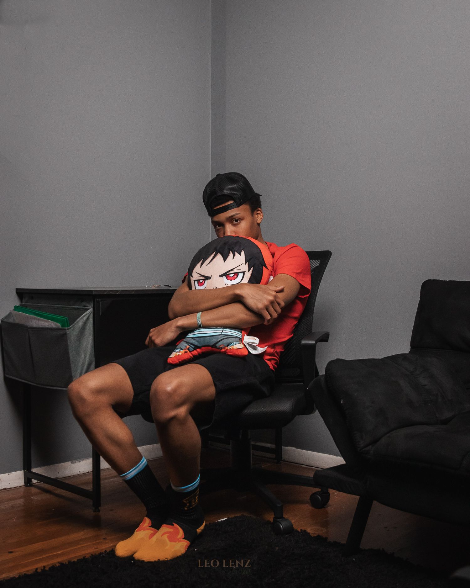 Person sitting in gaming chair holding anime character pillow in dimly lit room.