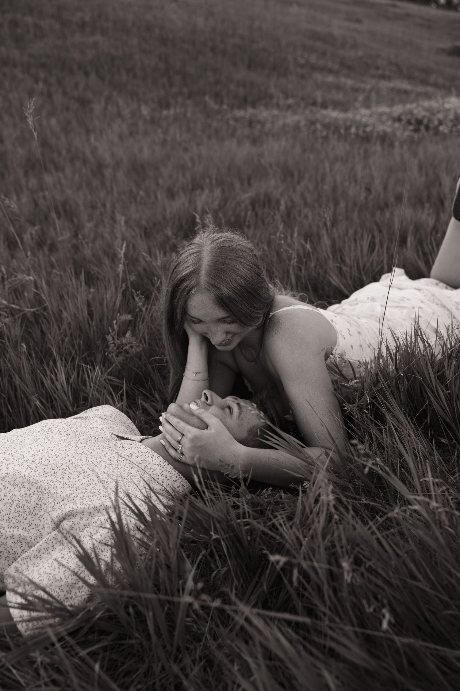 Black and white photo of two women lying in tall grass, sharing an intimate moment together.
