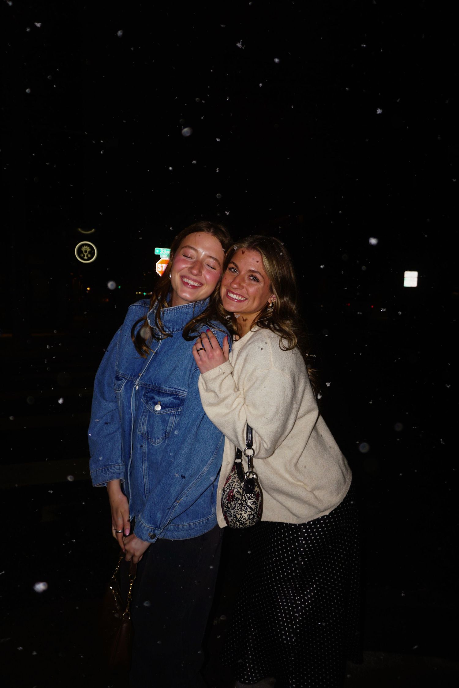 Two young women smiling and hugging outdoors at night in the snow.