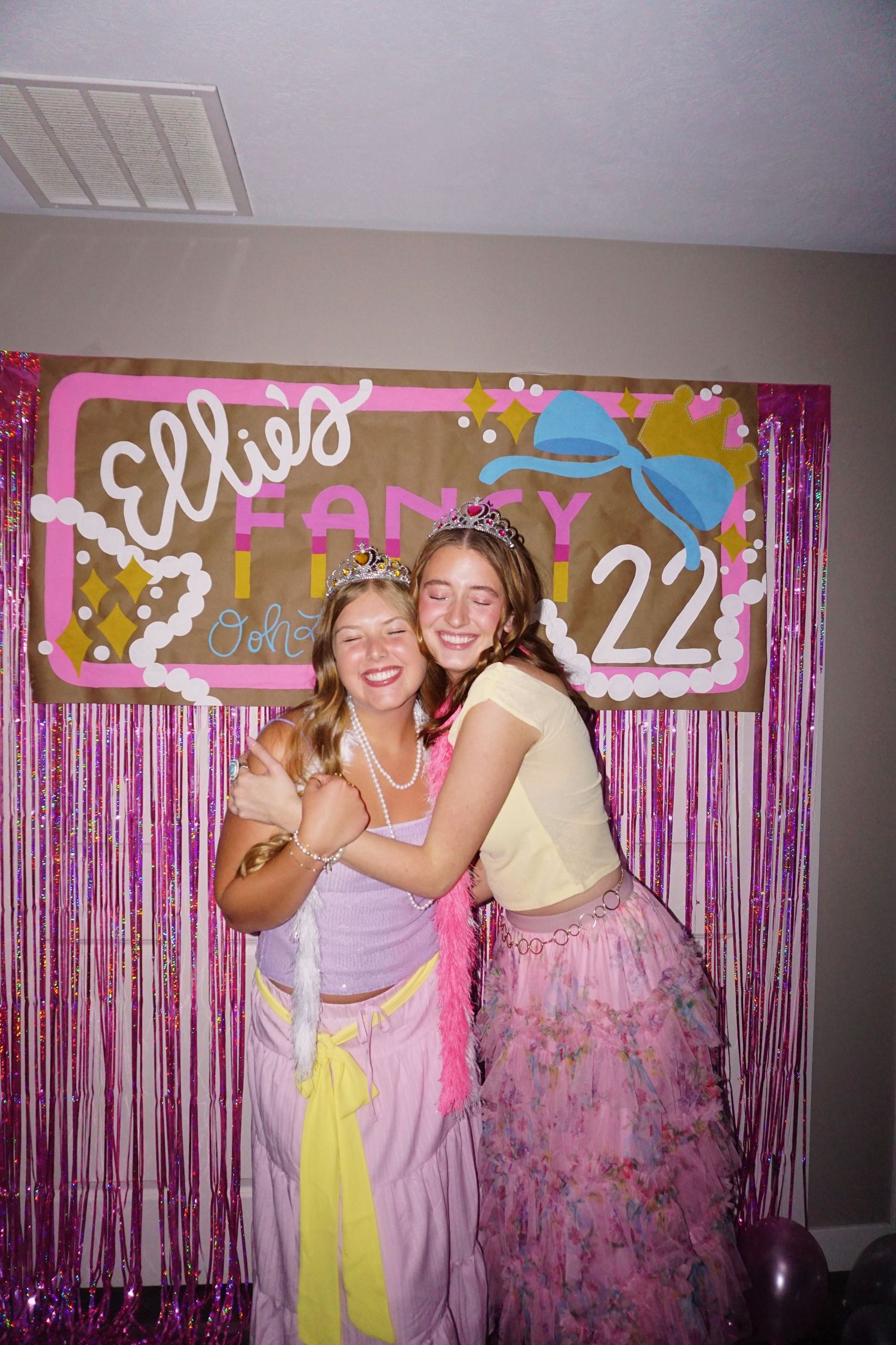 Two young women hugging and smiling in front of Ellies Fancy Lunch 22 birthday backdrop.