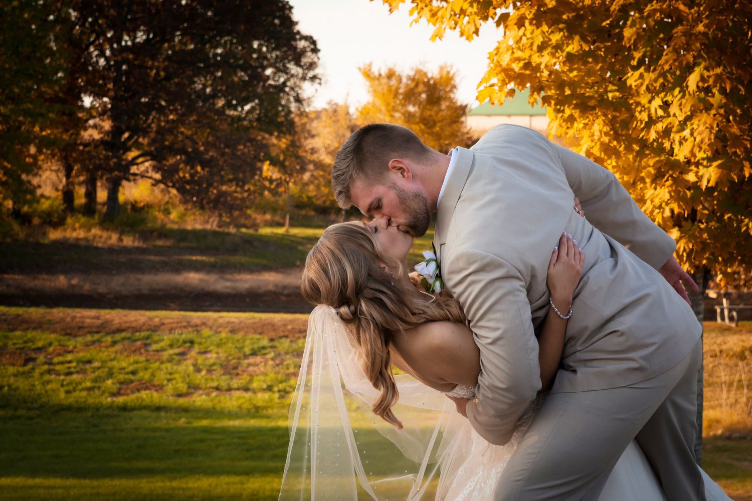 Romantic couple embraces during golden hour with autumn foliage in the background.