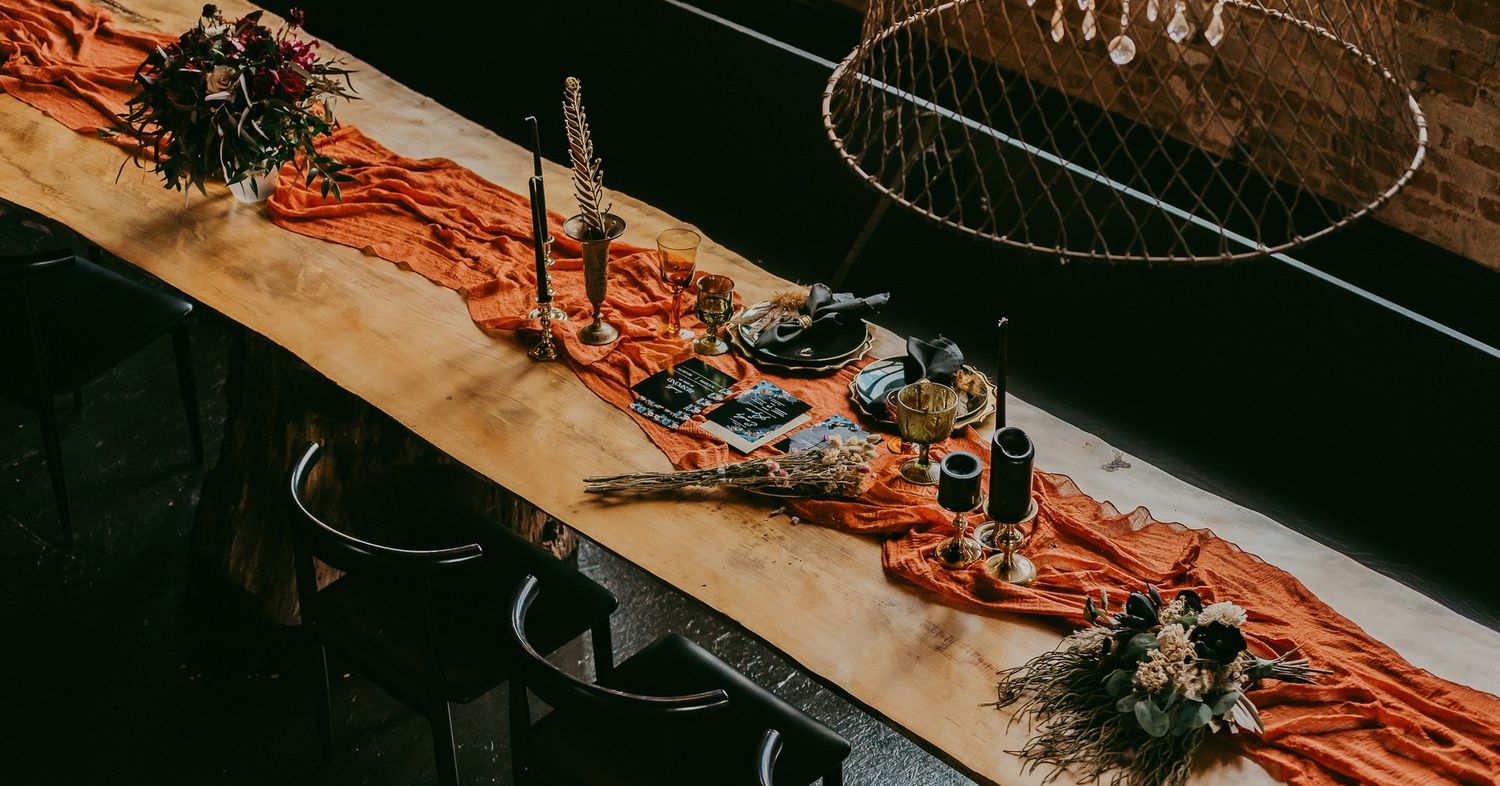 An elegant table setting with candles and floral decorations on an orange runner.