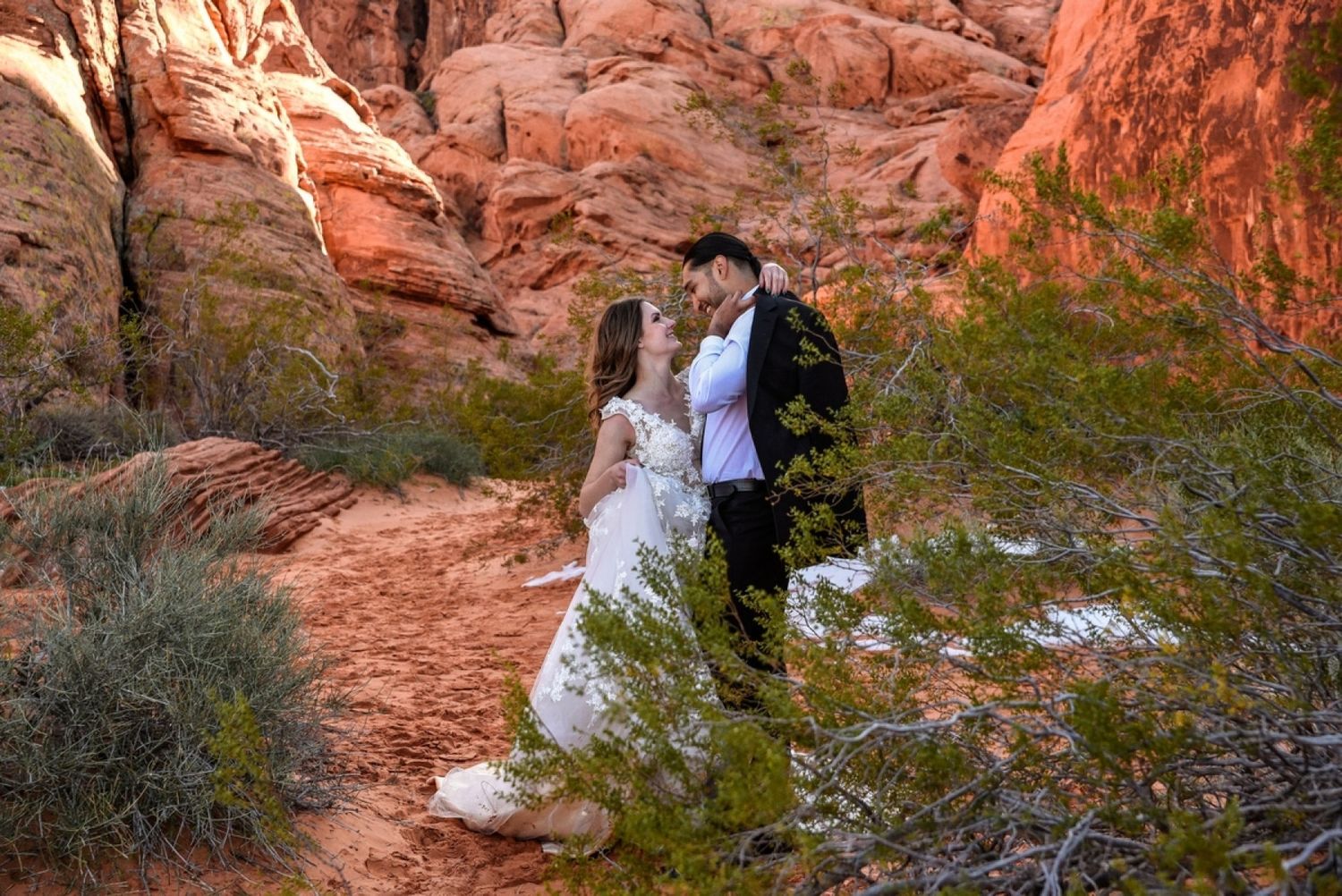 Wedding couple poses against dramatic red rock formations in a desert landscape.