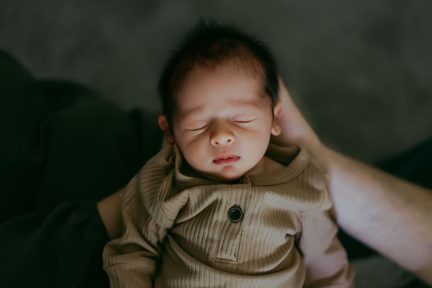 Candid newborn photography in moody lighting with brown tones.