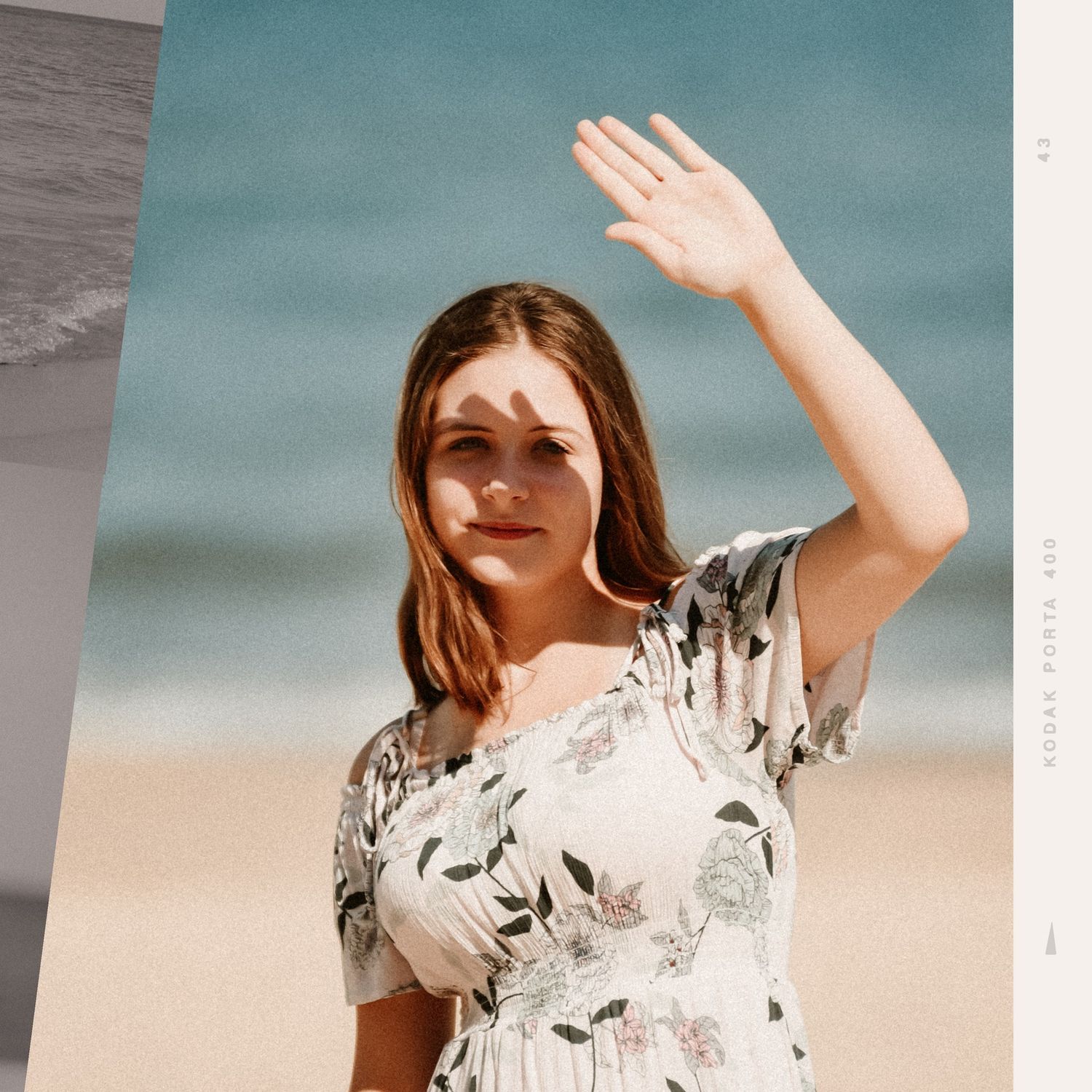 Woman in floral dress poses against beach backdrop in warm sunlight.