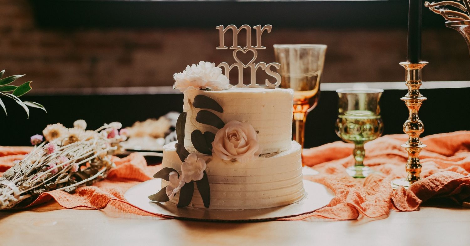 A white wedding cake with Mr and Mrs topper displayed on an orange table setting.
