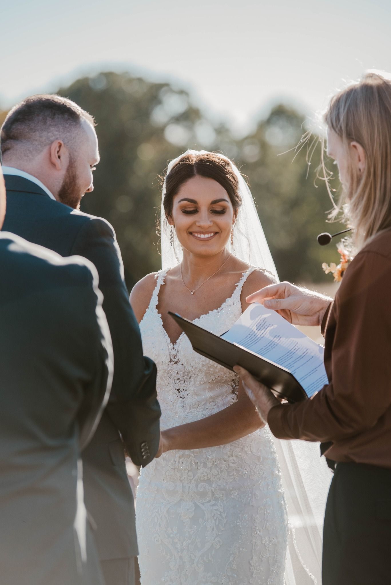 Outdoor wedding ceremony with couple and officiant during golden hour.