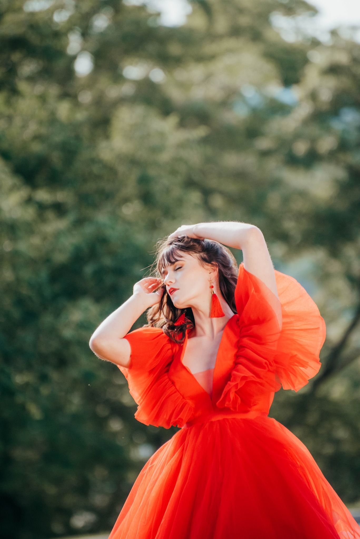 Woman in flowing red tulle dress twirling in dreamy outdoor setting.