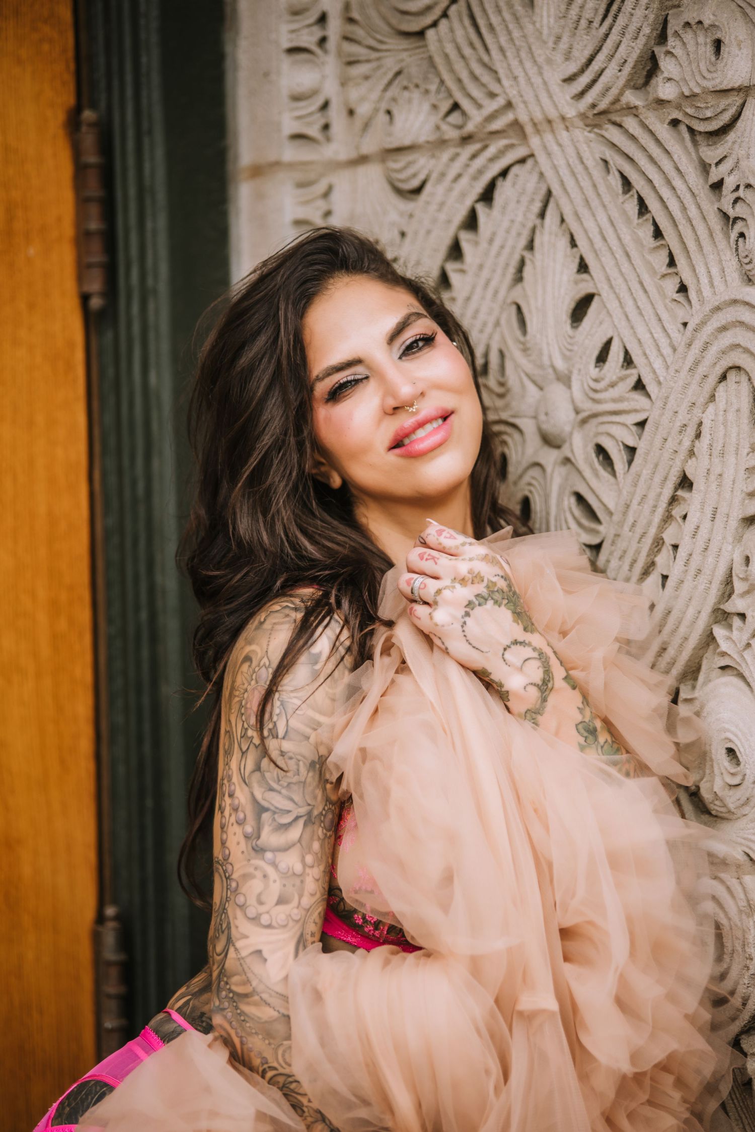 A dreamy portrait against an ornate wall featuring a flowing peach-colored dress.
