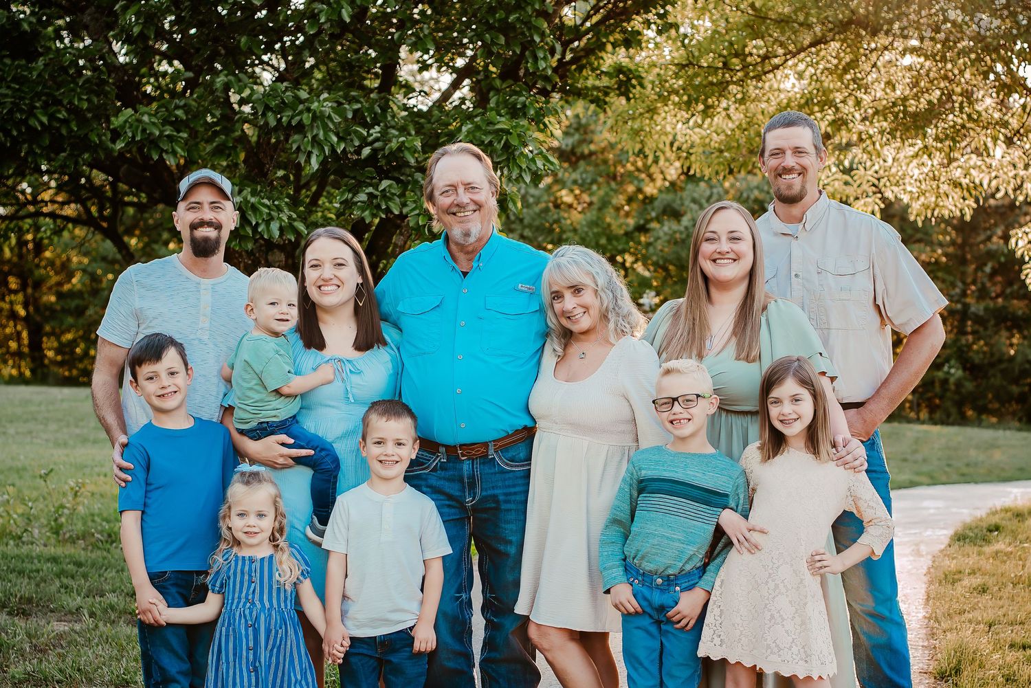 Large multigenerational family posing together outdoors on a green lawn with trees in the background.