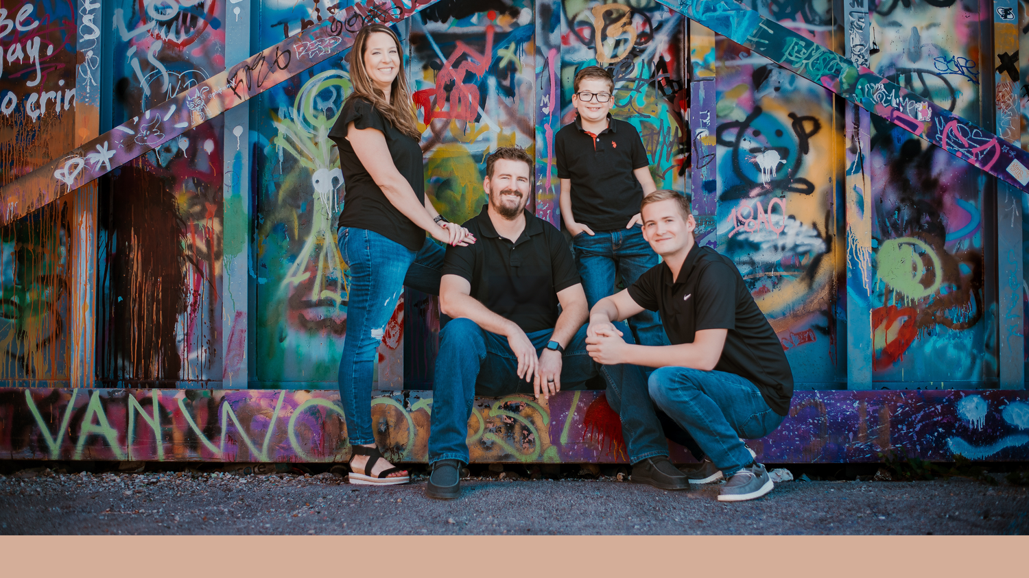 Four people in black shirts pose in front of a vibrant graffiti wall for a fun group photo.