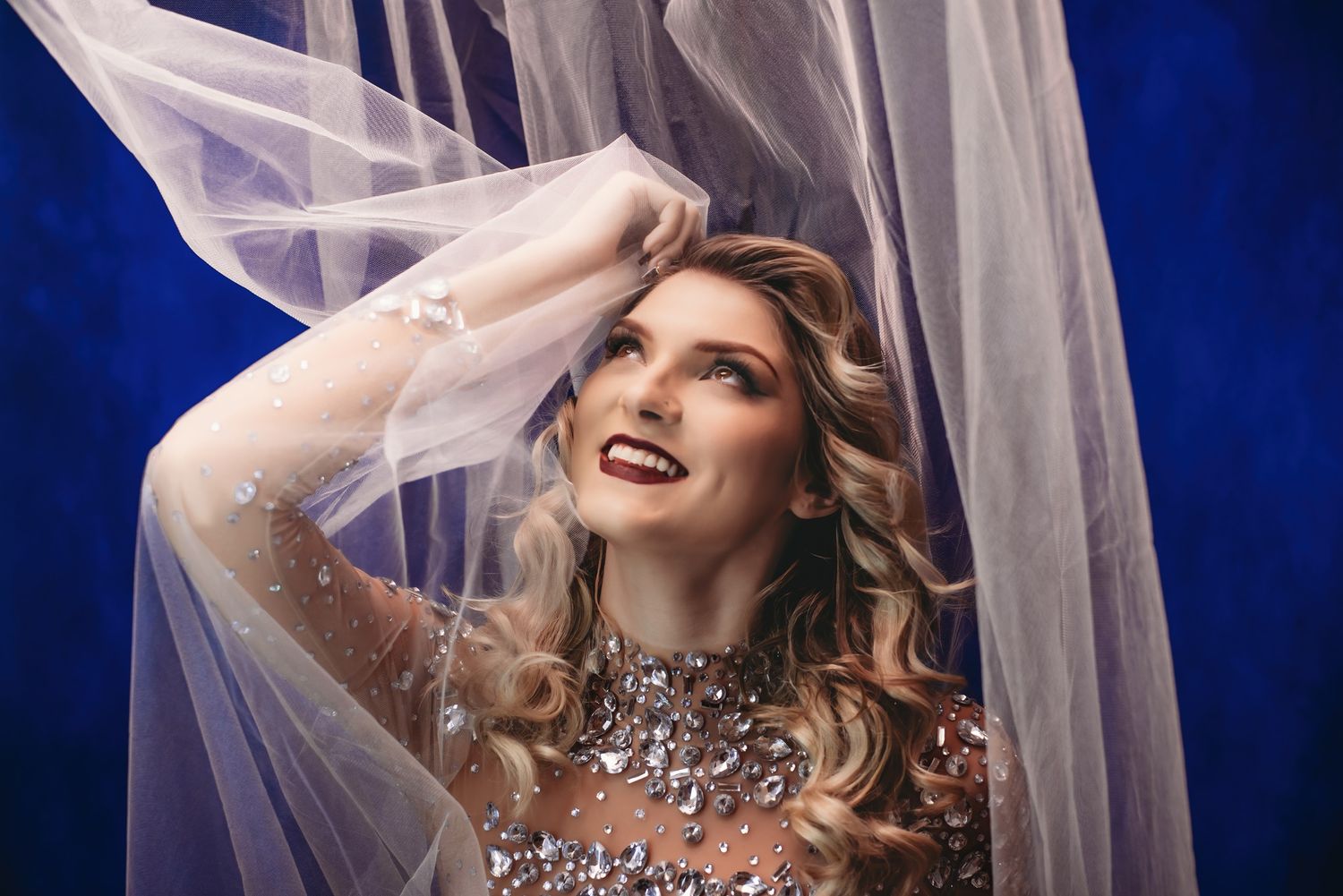 Ethereal bridal portrait with flowing veil against deep blue background.