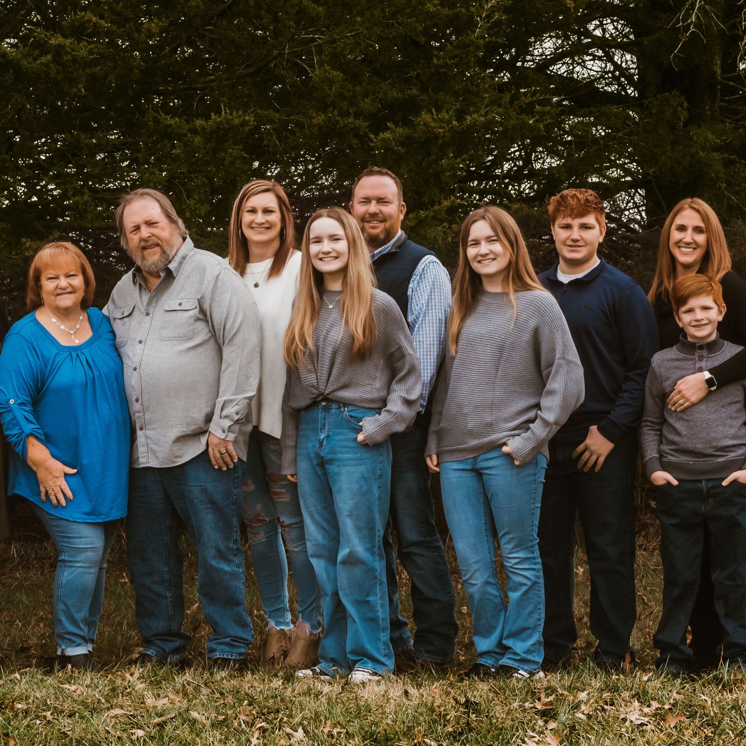 Large family group wearing coordinating blue and grey outfits poses casually outdoors.