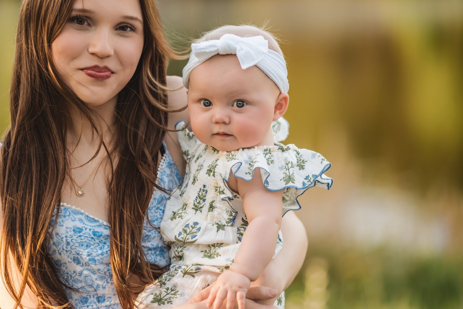 Parent and baby wearing matching floral outfits pose together in outdoor setting with soft bokeh background.