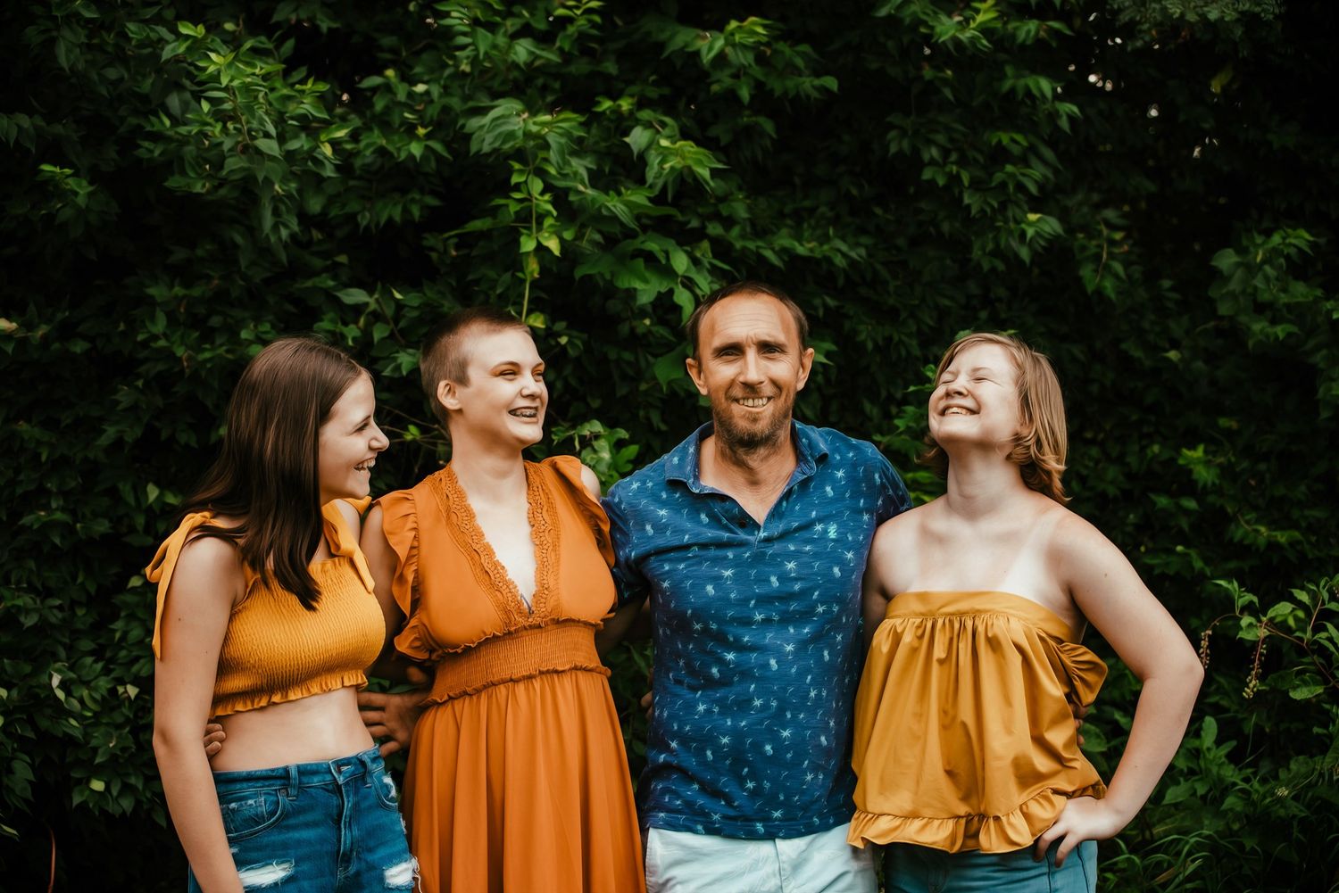 Group portrait in casual summer attire against lush green foliage.