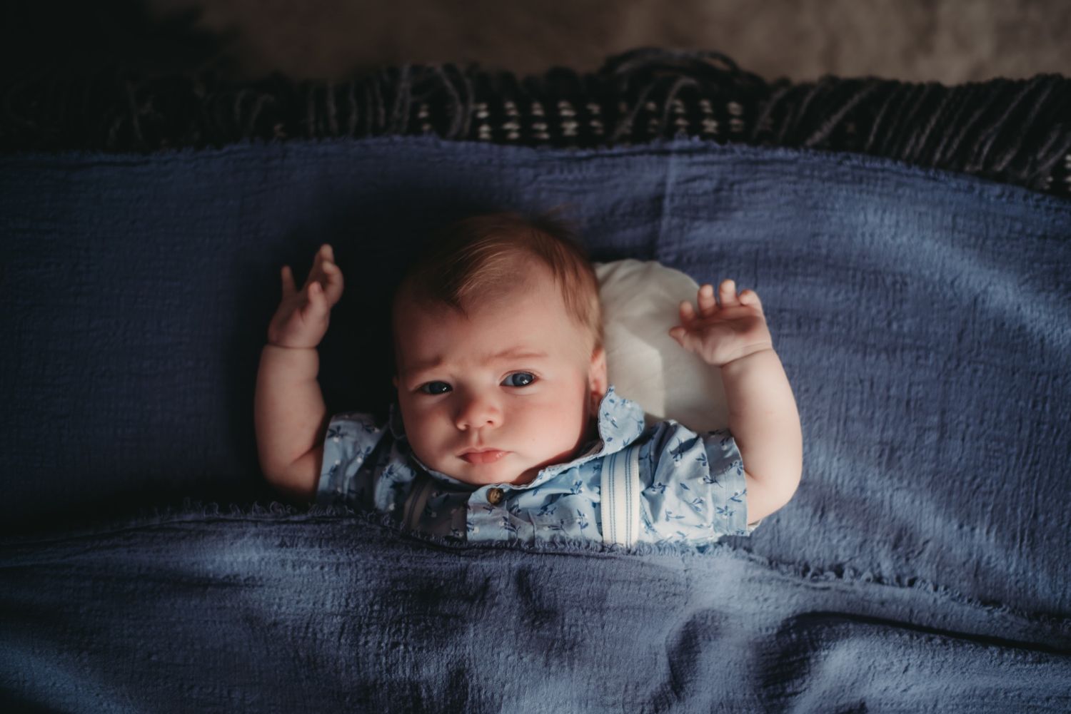 A sleeping infant lies peacefully under soft blue blankets in natural light.