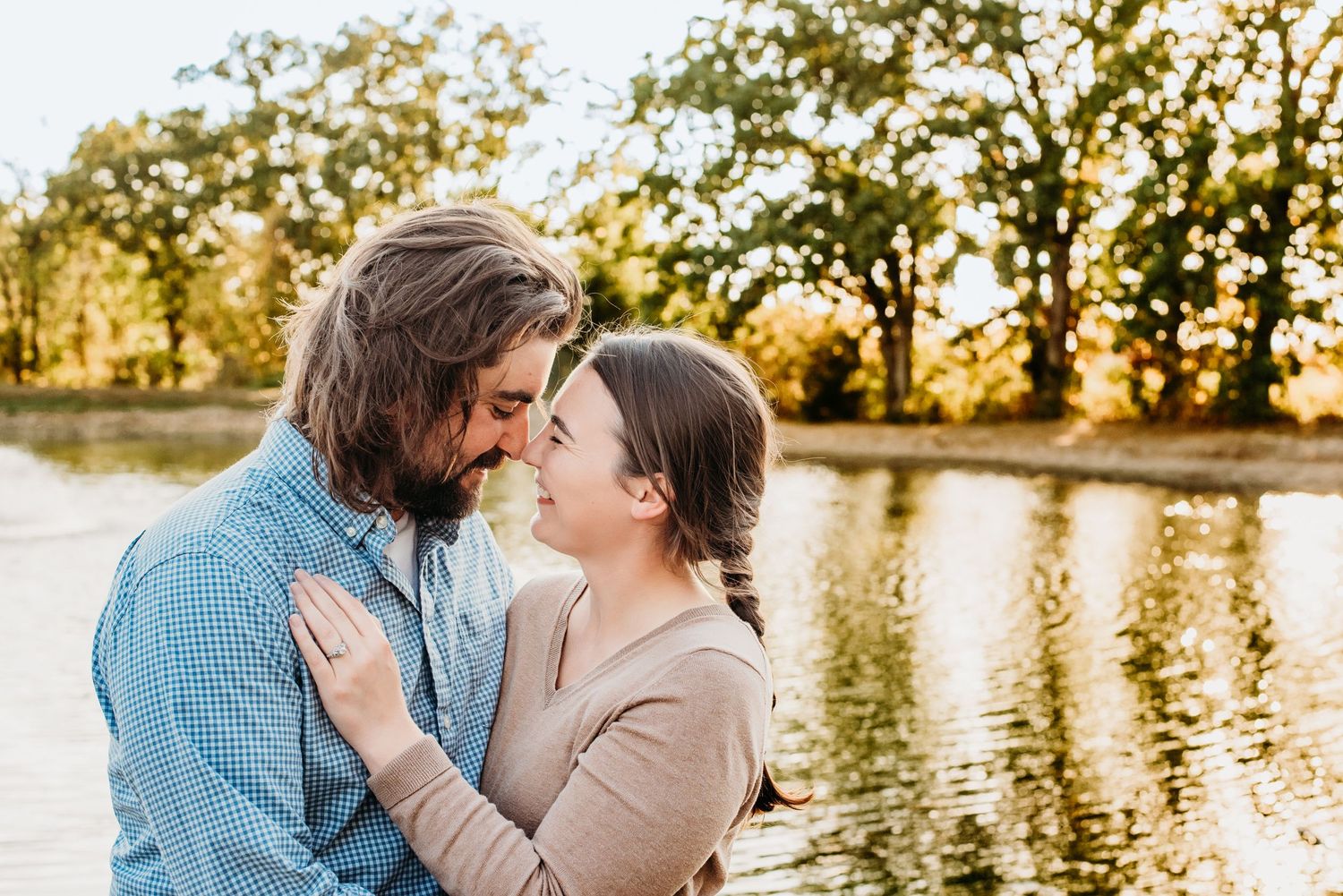 Romantic couple embracing during golden hour with sunlit trees in background.