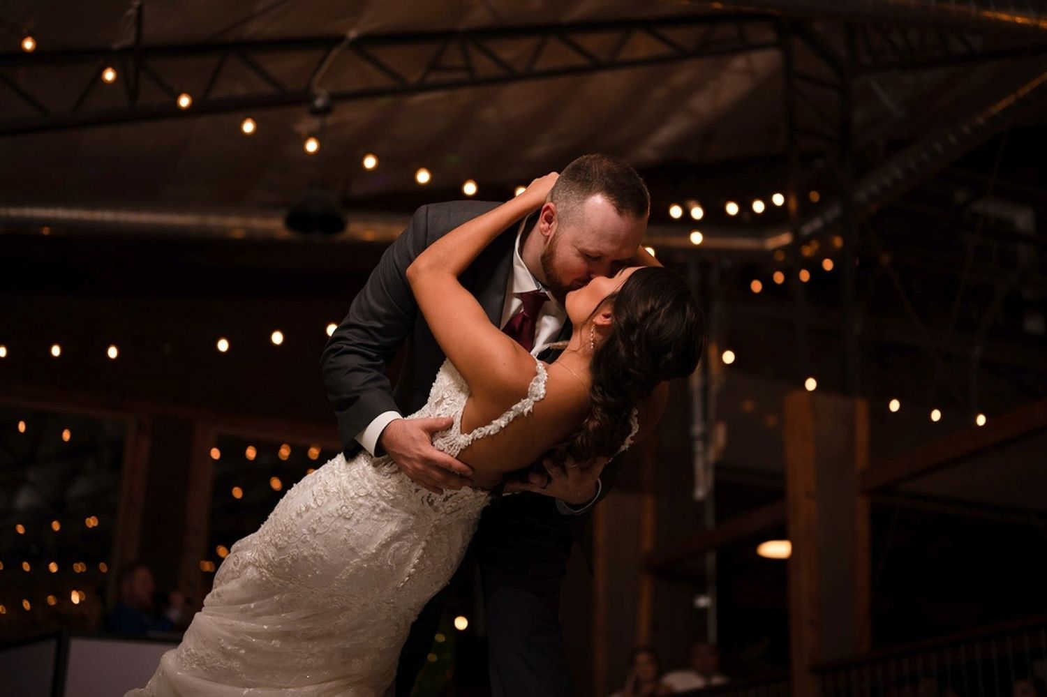Romantic dance moment under string lights at indoor wedding reception.