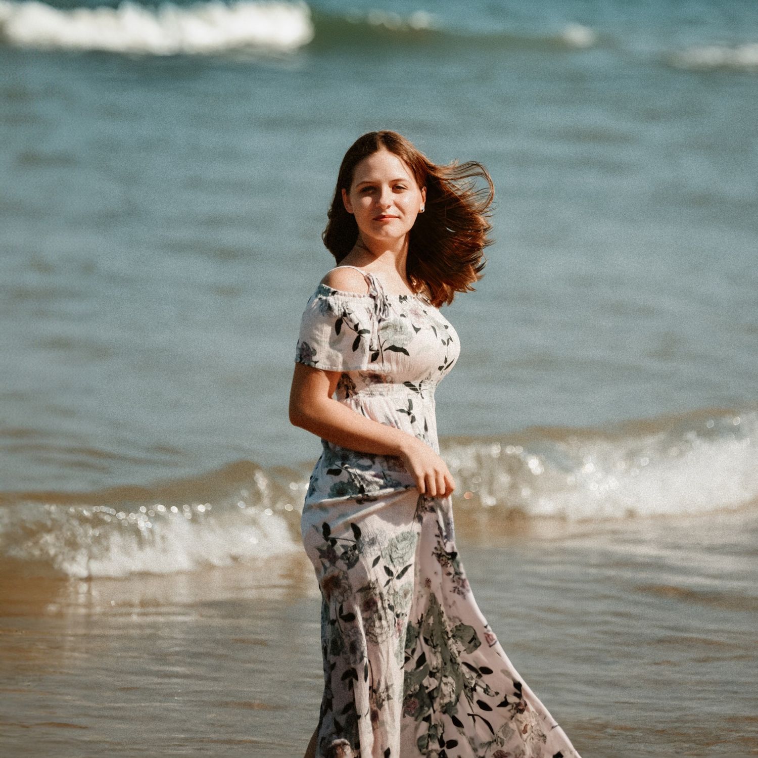Person in floral dress twirling joyfully on sunny beach.