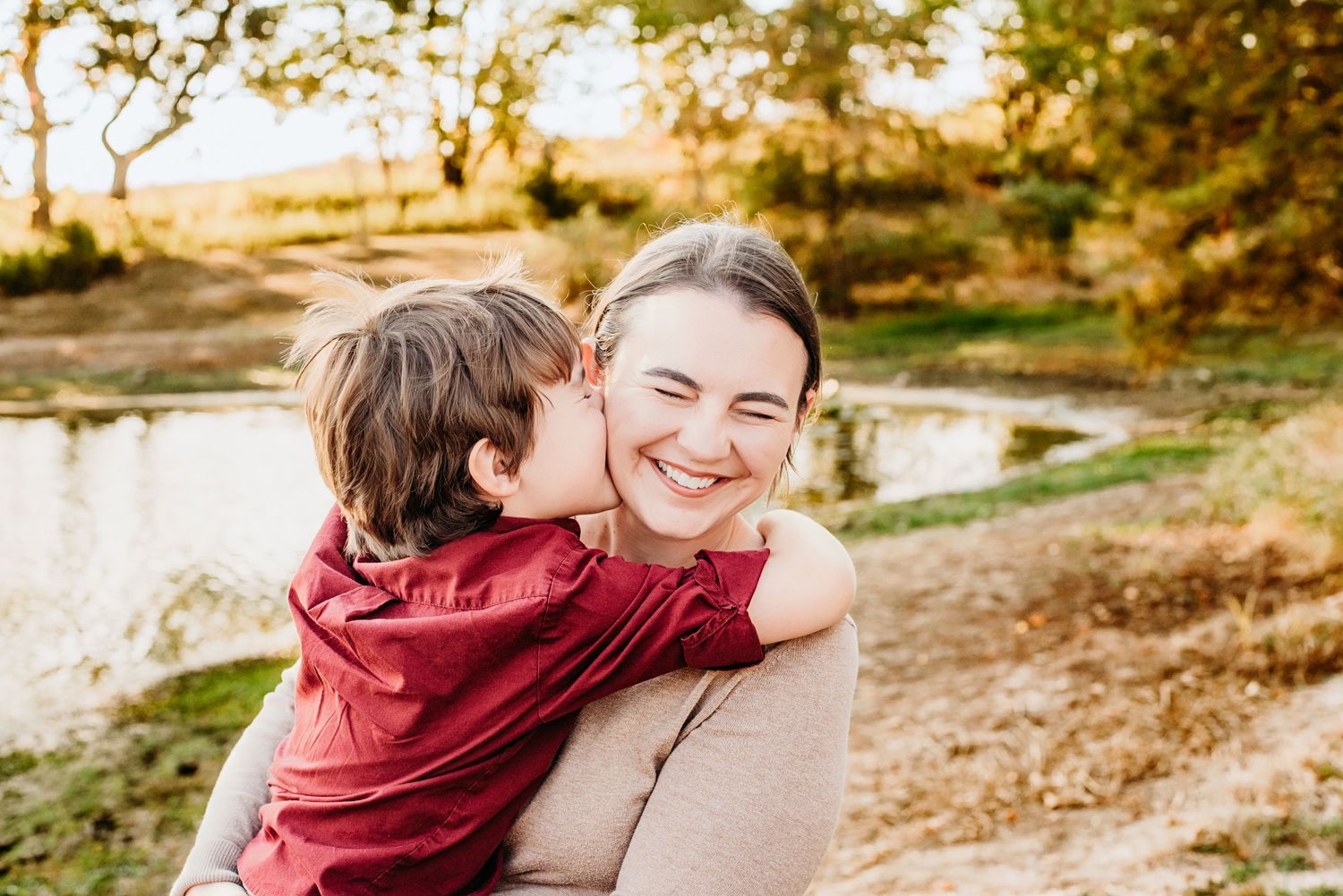 A couple in burgundy sweaters share tender moments together during an autumn photoshoot near a lake.