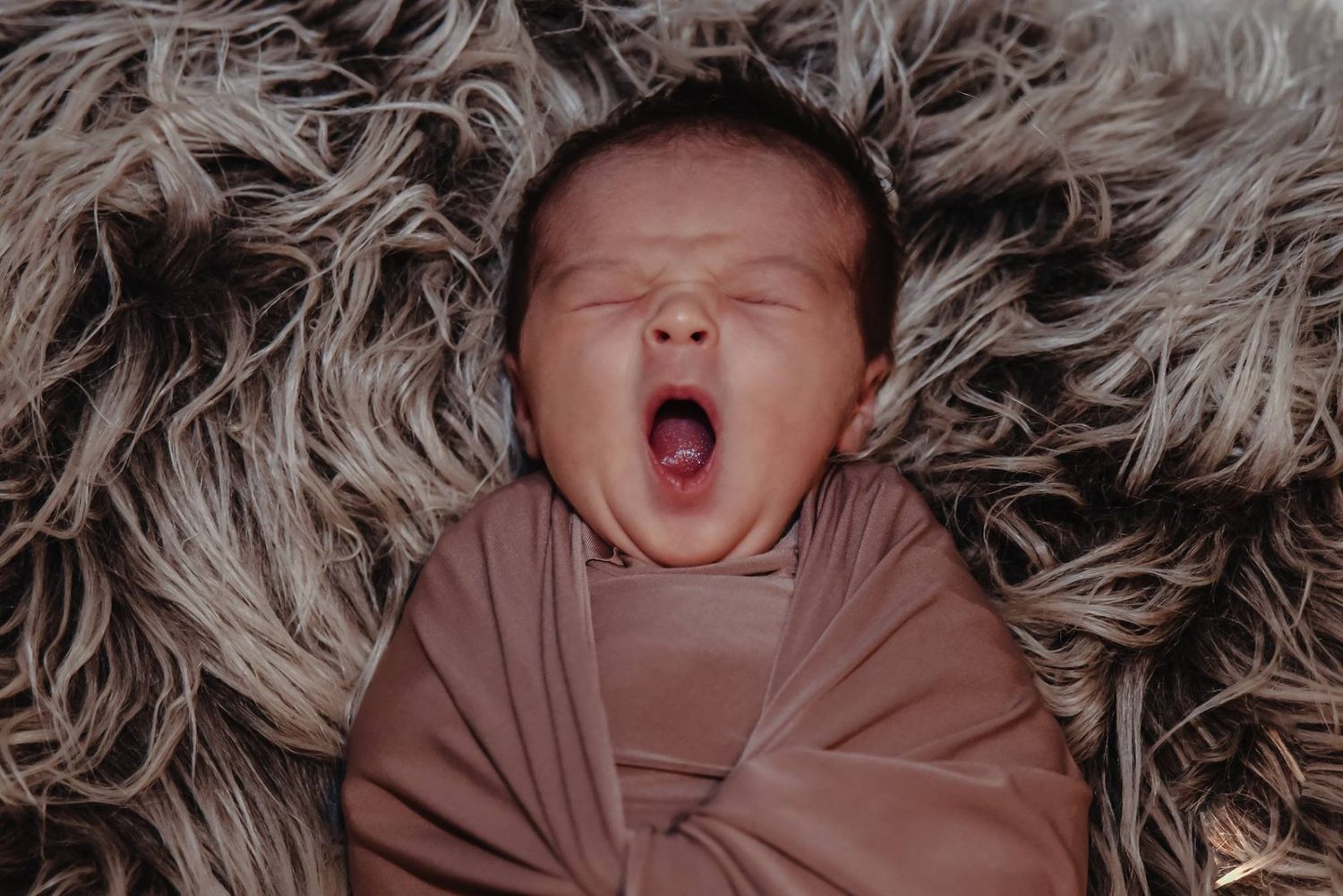 Newborn baby sleeping on soft textured blanket in muted tones.