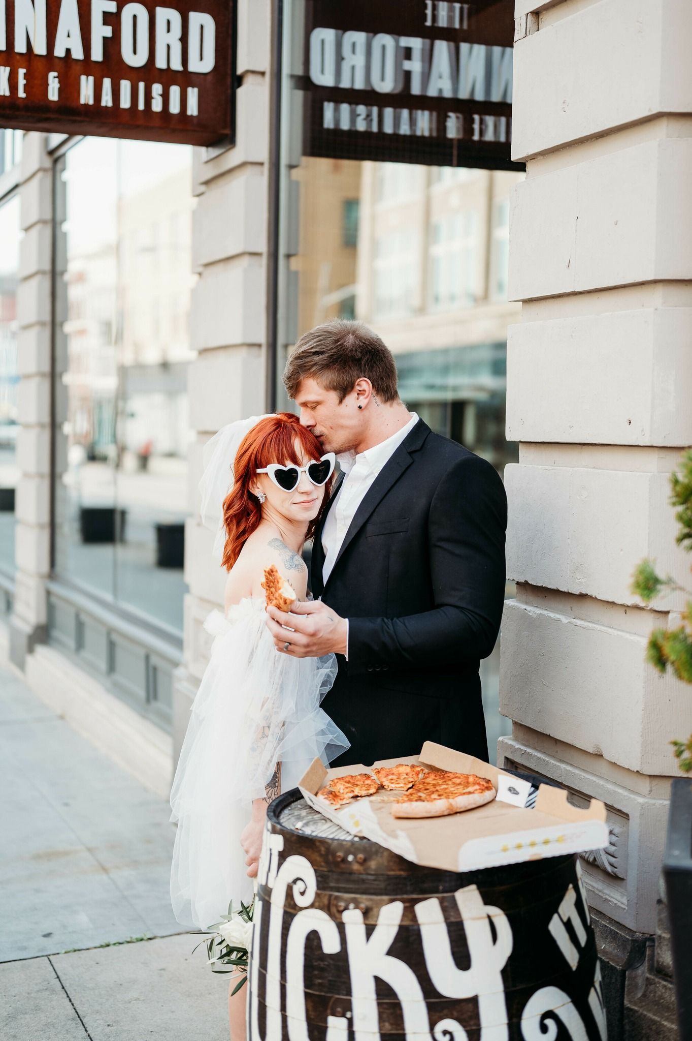 Couple sharing pizza and romantic moments outside an urban storefront.