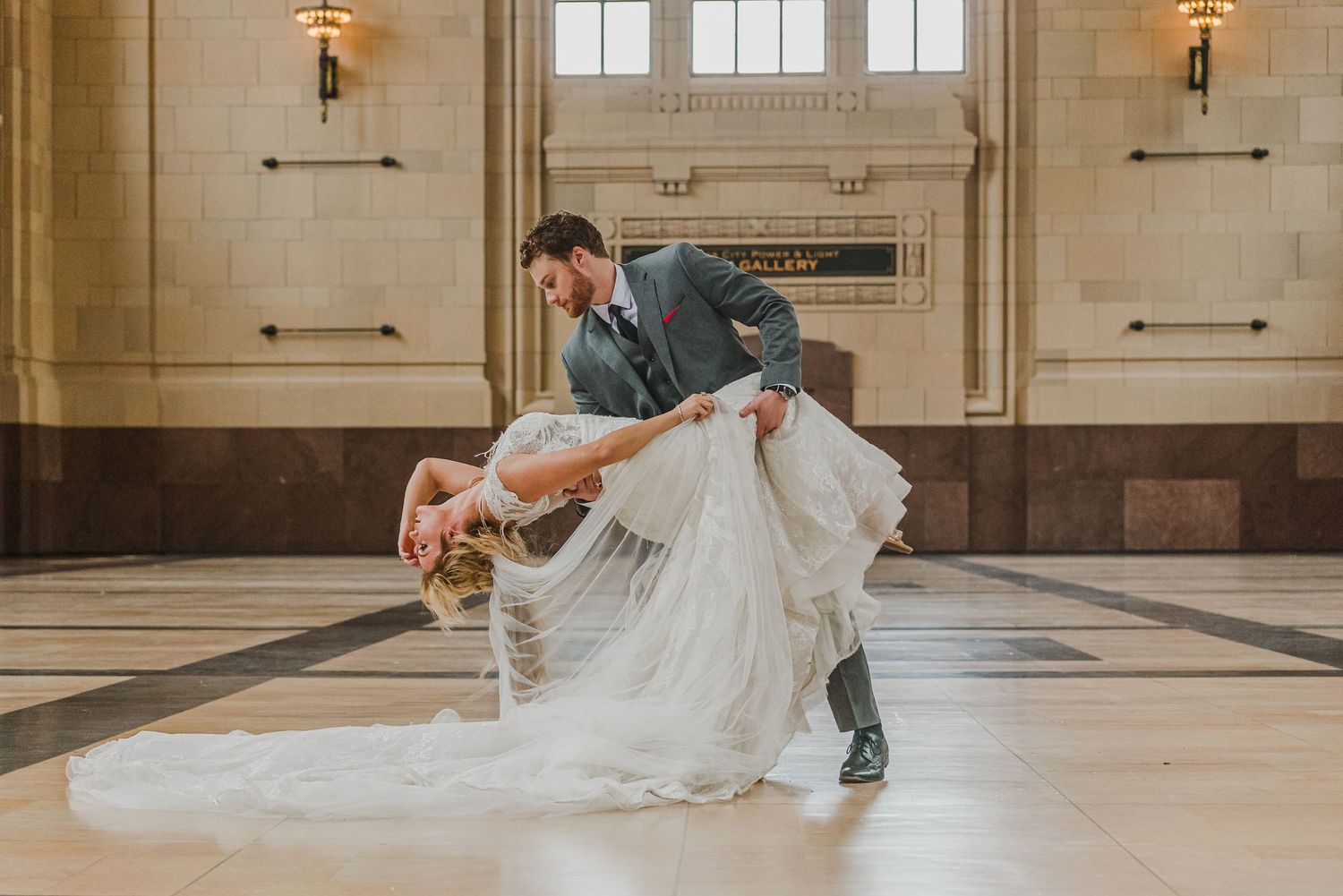 Romantic dance dip pose in grand historic building interior with elegant wedding attire.
