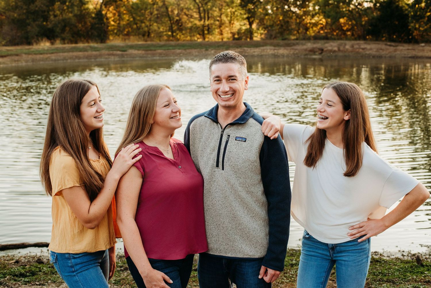 Group of young people laughing together by lake during autumn sunset.