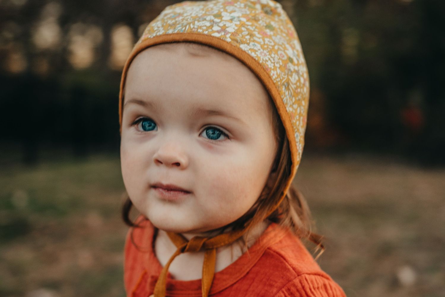 Close up portrait of child wearing orange sweater and patterned headband outdoors.