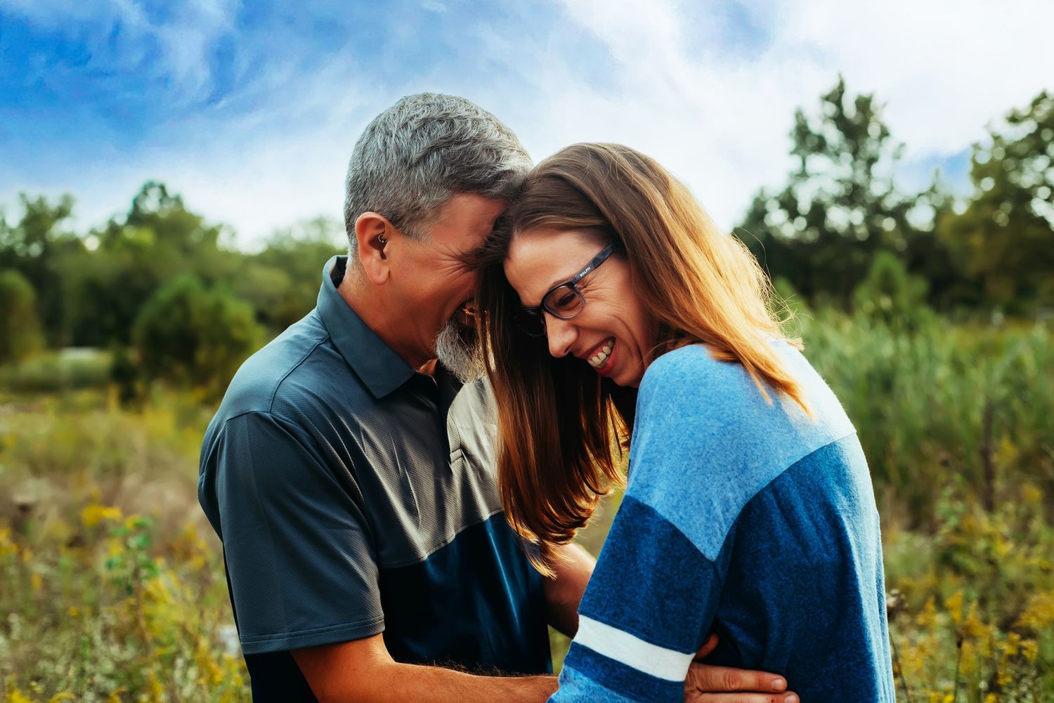 Couple embracing outdoors in a field on a sunny day wearing blue and casual attire.