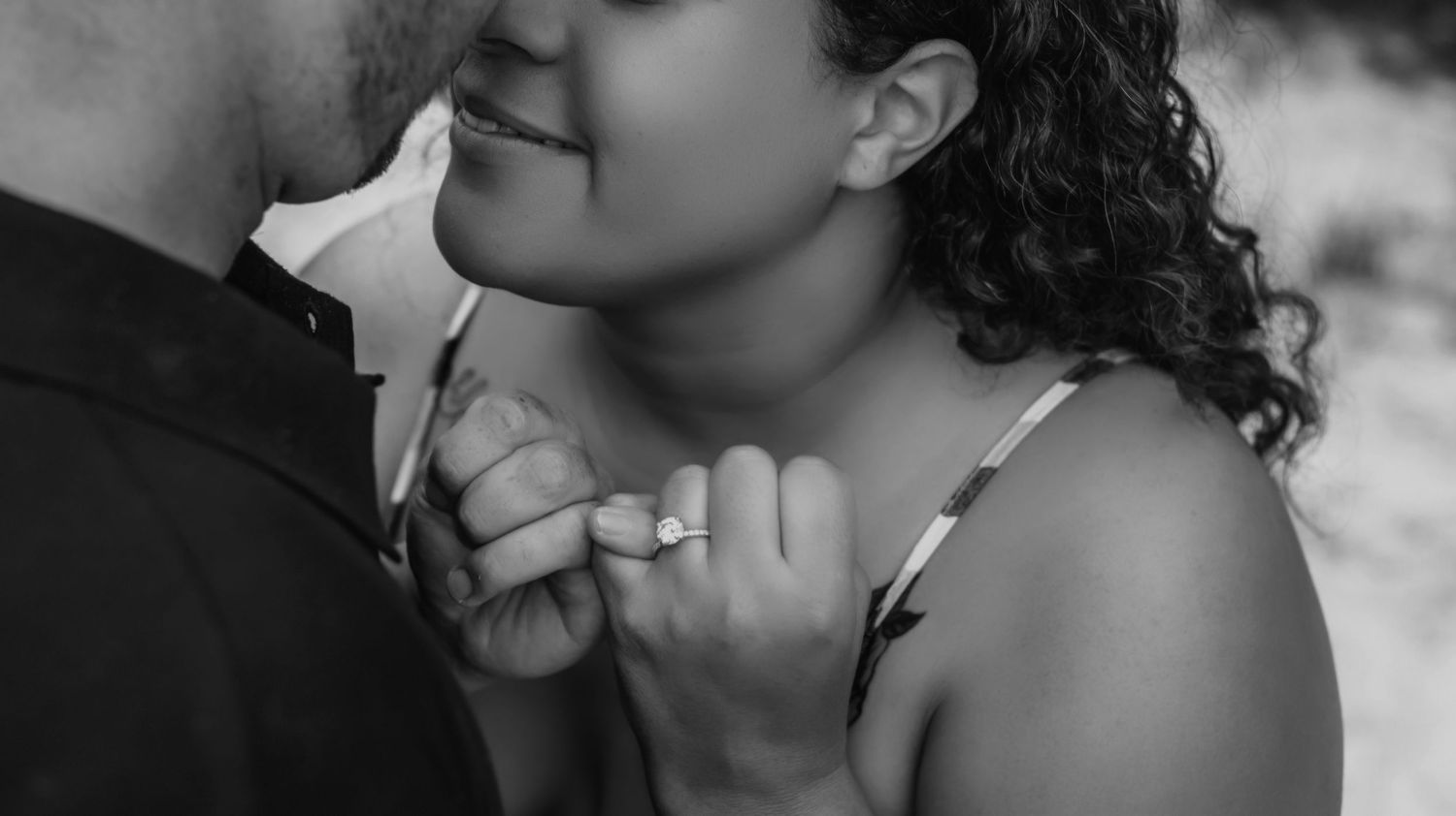 Black and white intimate portrait showing tender embrace with curly hair and gentle smile.