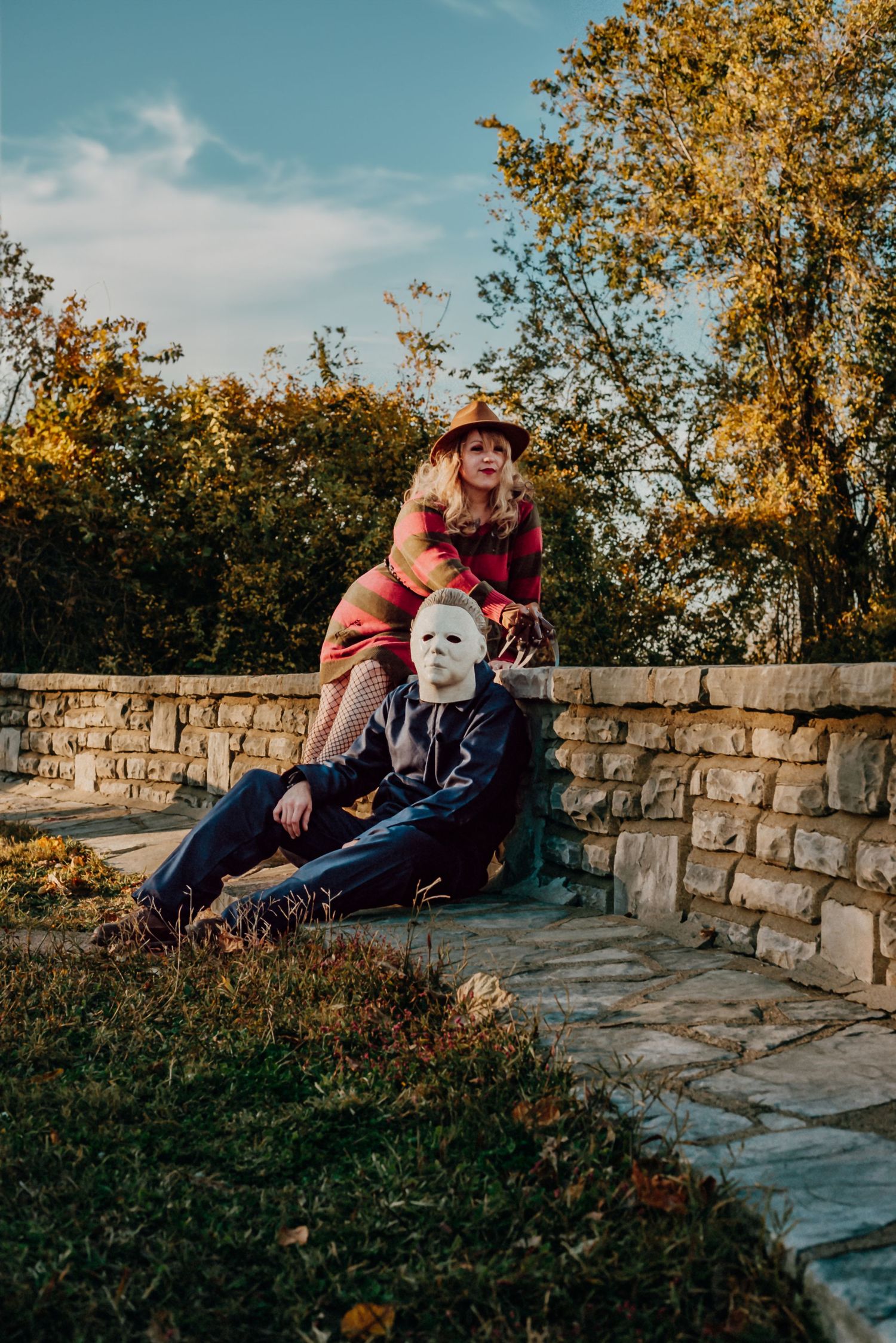 Halloween-themed portrait with people in costumes sitting on stone wall at sunset.