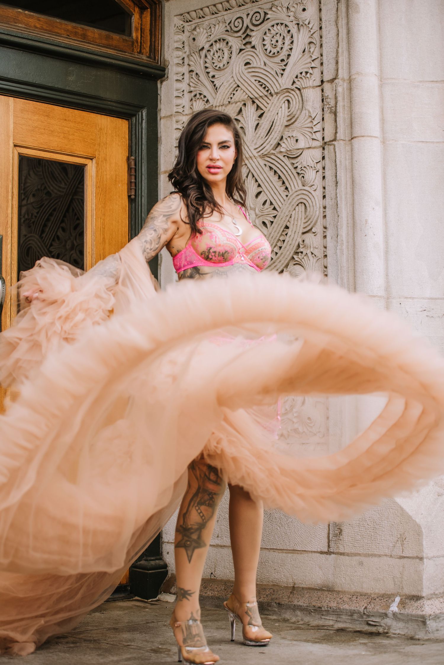 Woman in flowing peach gown twirling against ornate architectural backdrop.