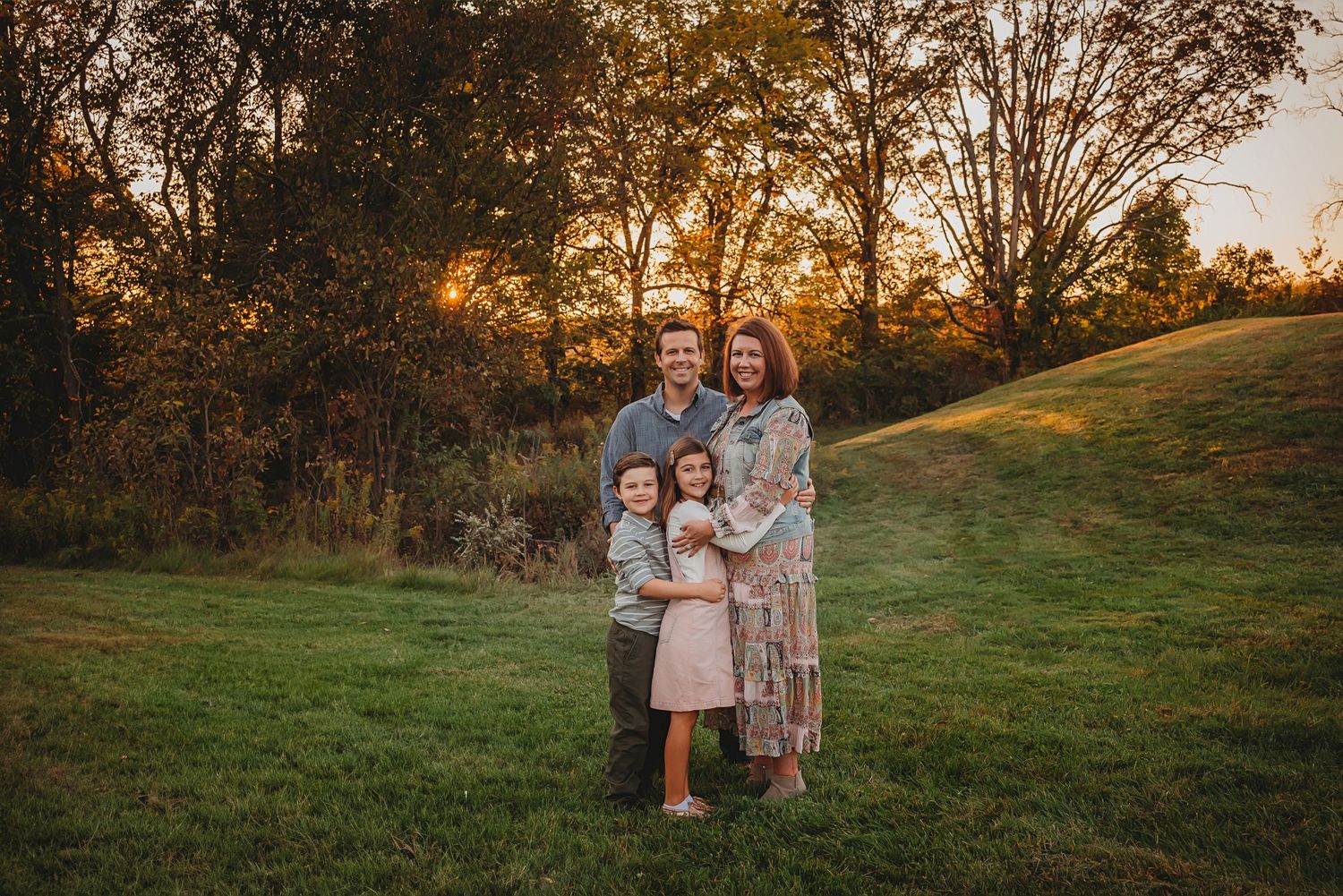 Family portrait at sunset in a grassy field with golden autumn light.