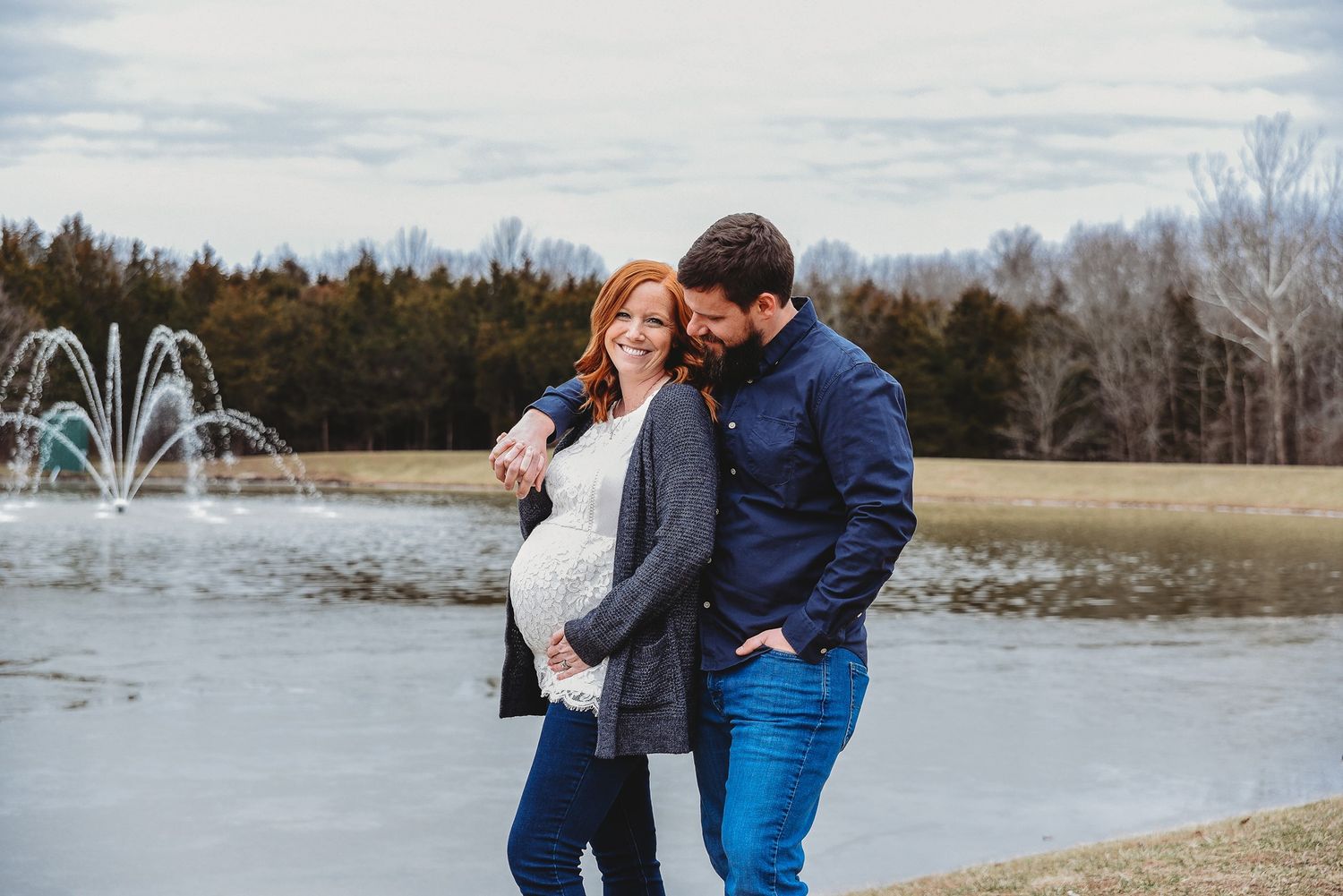 A couple shares intimate moments by a lake with fountain sprays in the background.